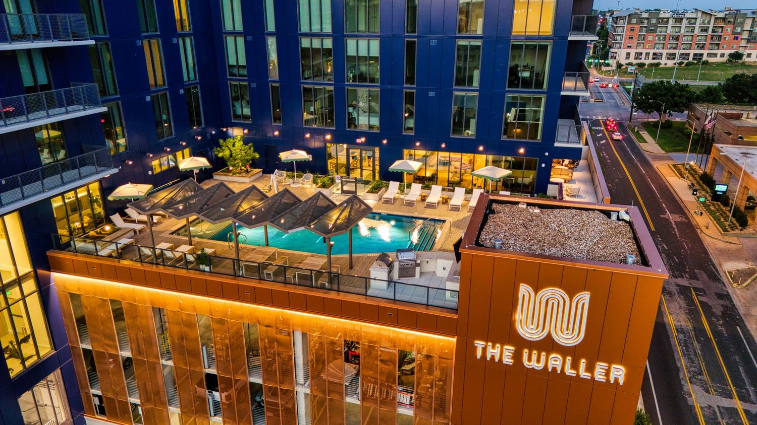 Dusk aerial shot of The Waller apartment building's rooftop pool deck with city views.