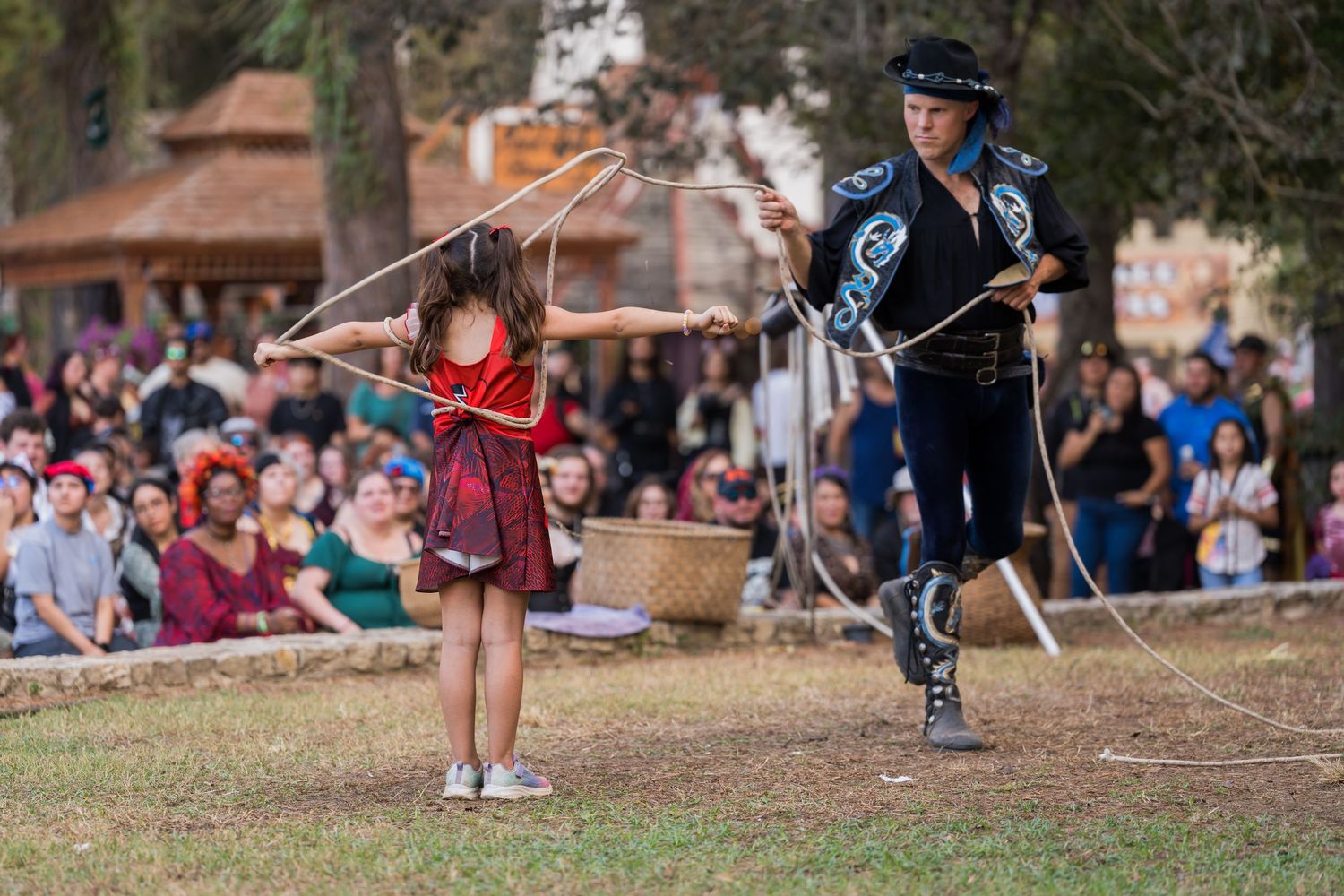 A sword fighting demonstration between performers on a grassy field at a Renaissance festival.