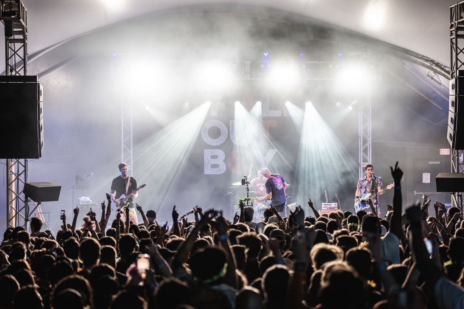 Silhouetted concert crowd facing illuminated stage with bright white lighting and fog effects.