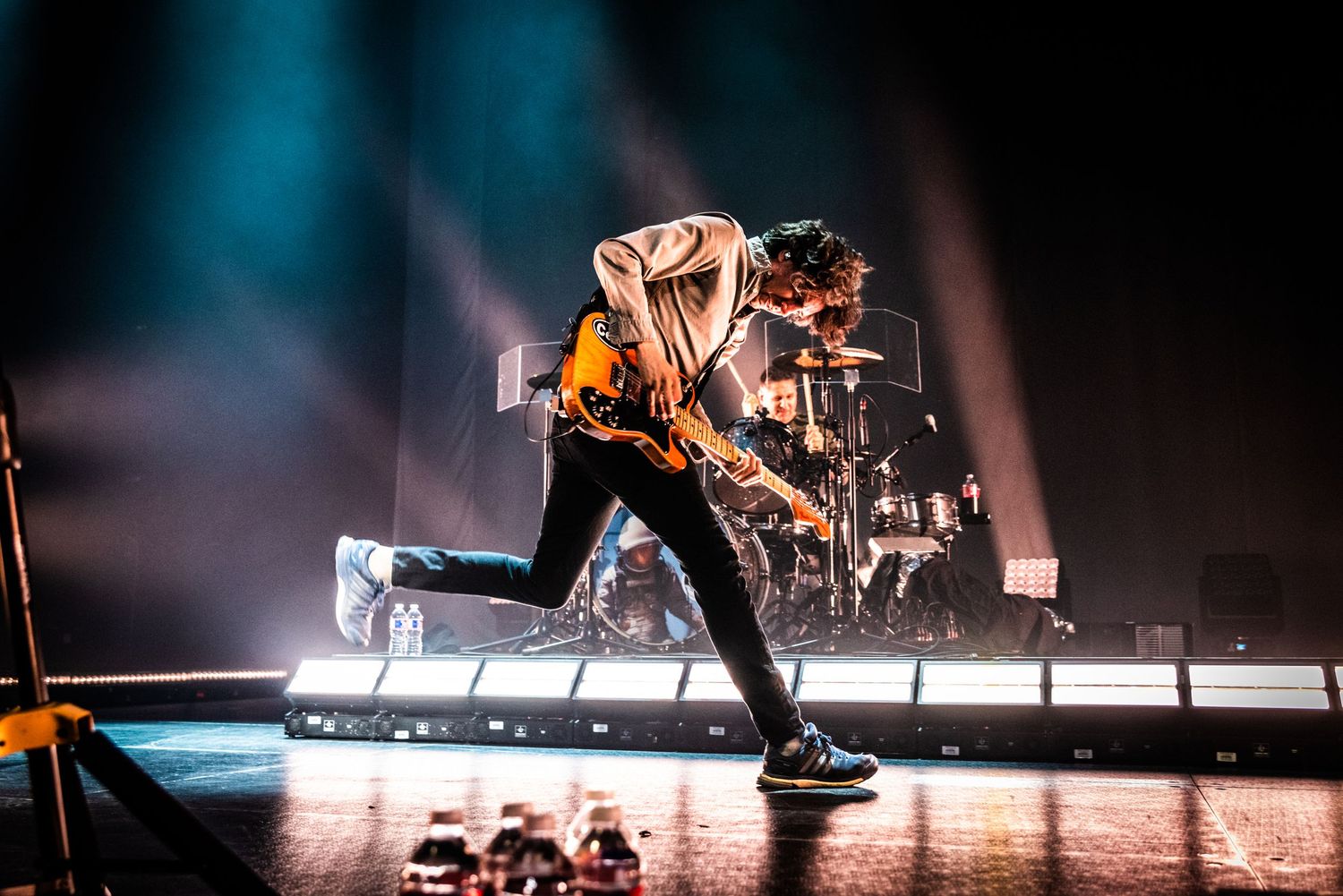 High-energy concert photo showing performer in dramatic stance on illuminated platform.