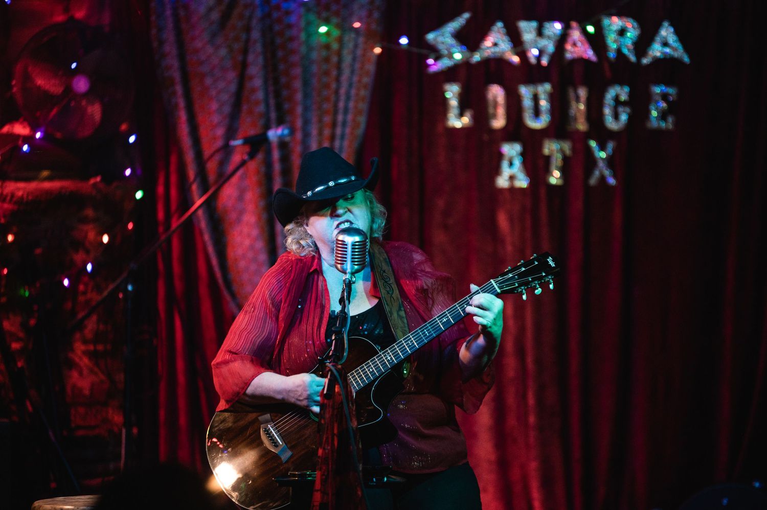 Musician performs at Sahara Lounge ATX venue with guitar under red stage lighting.