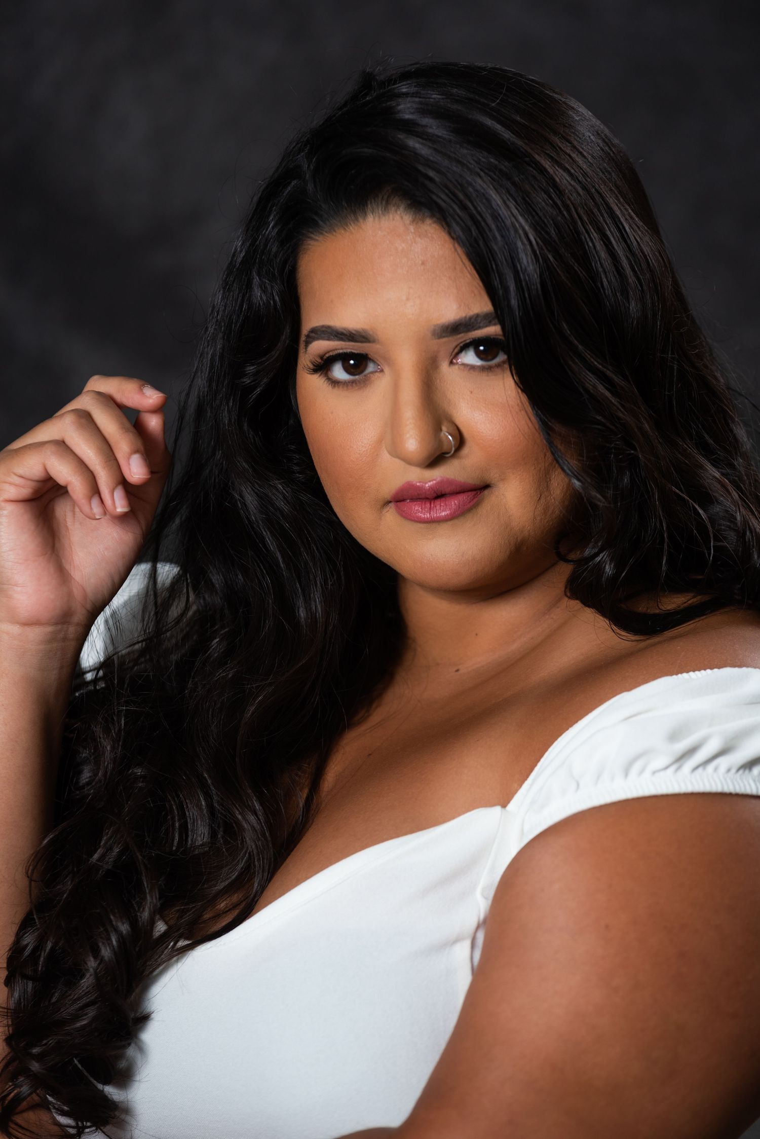 Beauty portrait in white top showing confident pose against dark background.