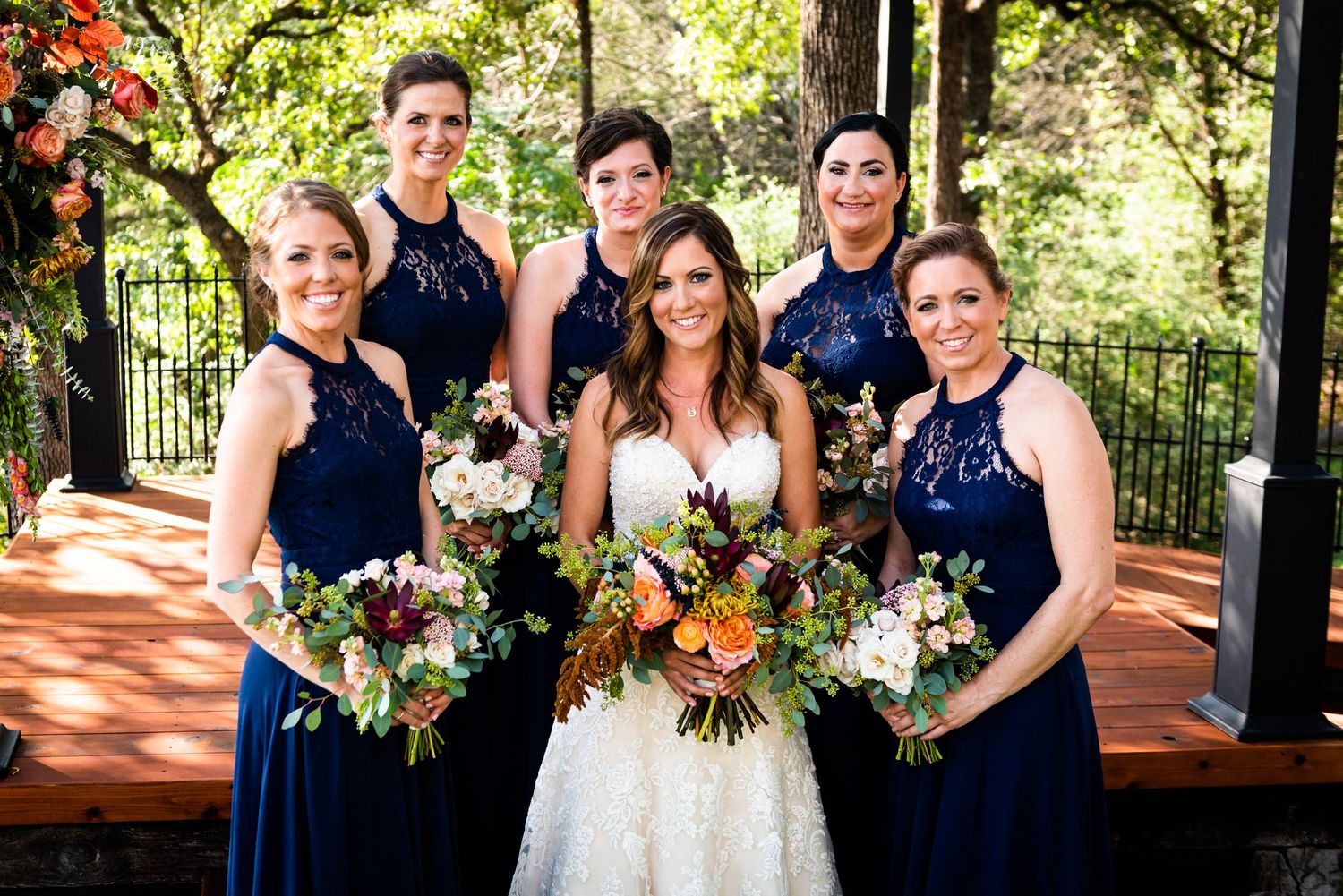 Wedding party in navy dresses poses with colorful bouquets on an outdoor terrace.