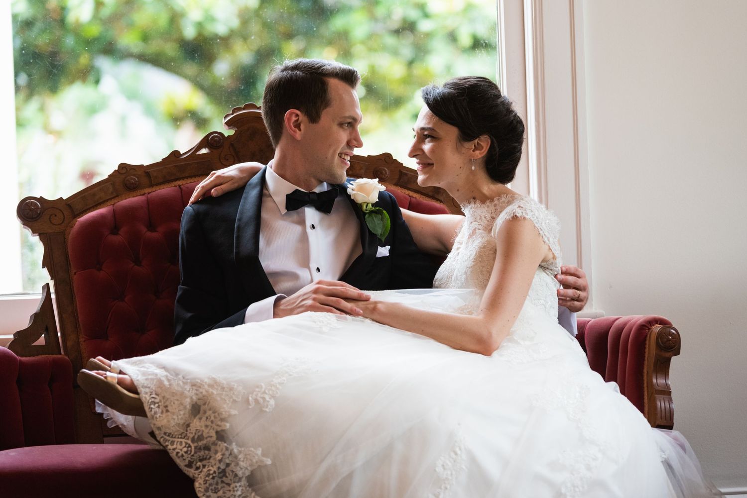 A romantic wedding portrait showing intimacy on a burgundy velvet couch.