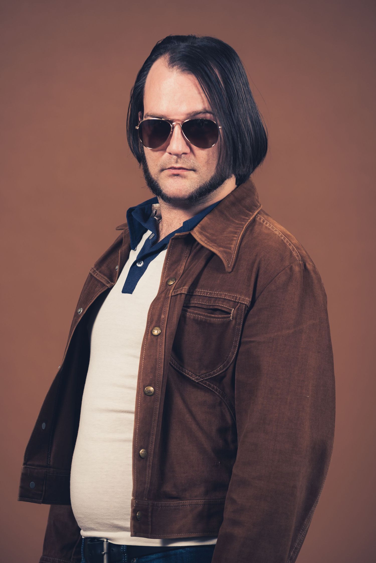 Person in brown jacket and sunglasses posing against brown background.