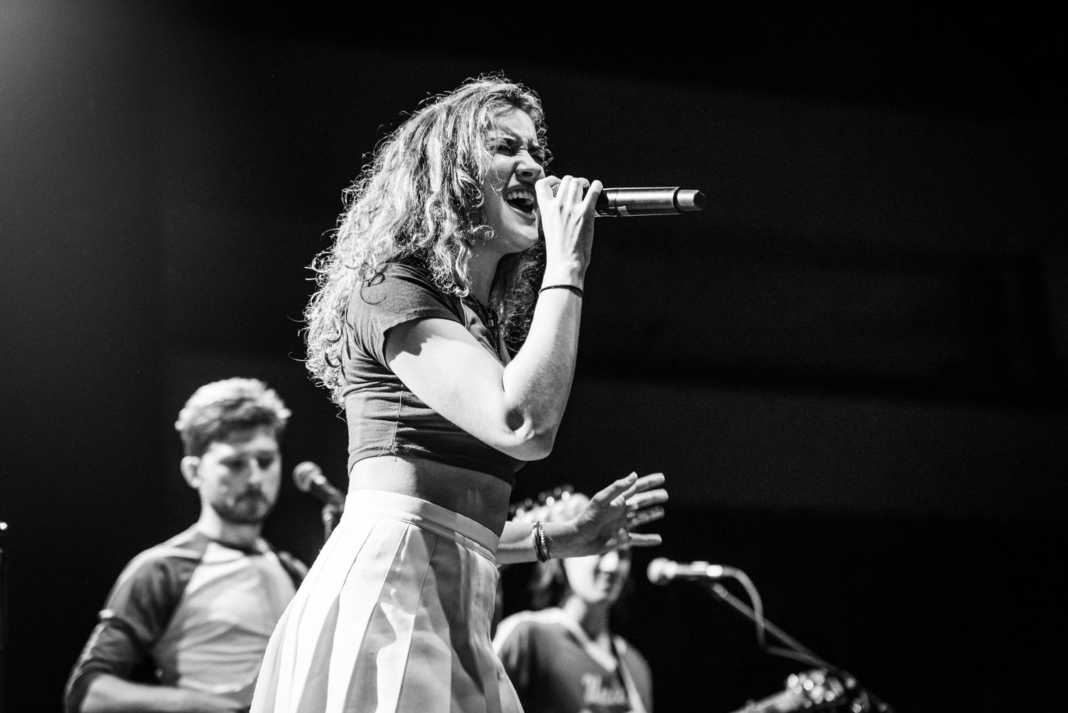 Energetic live music performance with singer and band members on stage in black and white.
