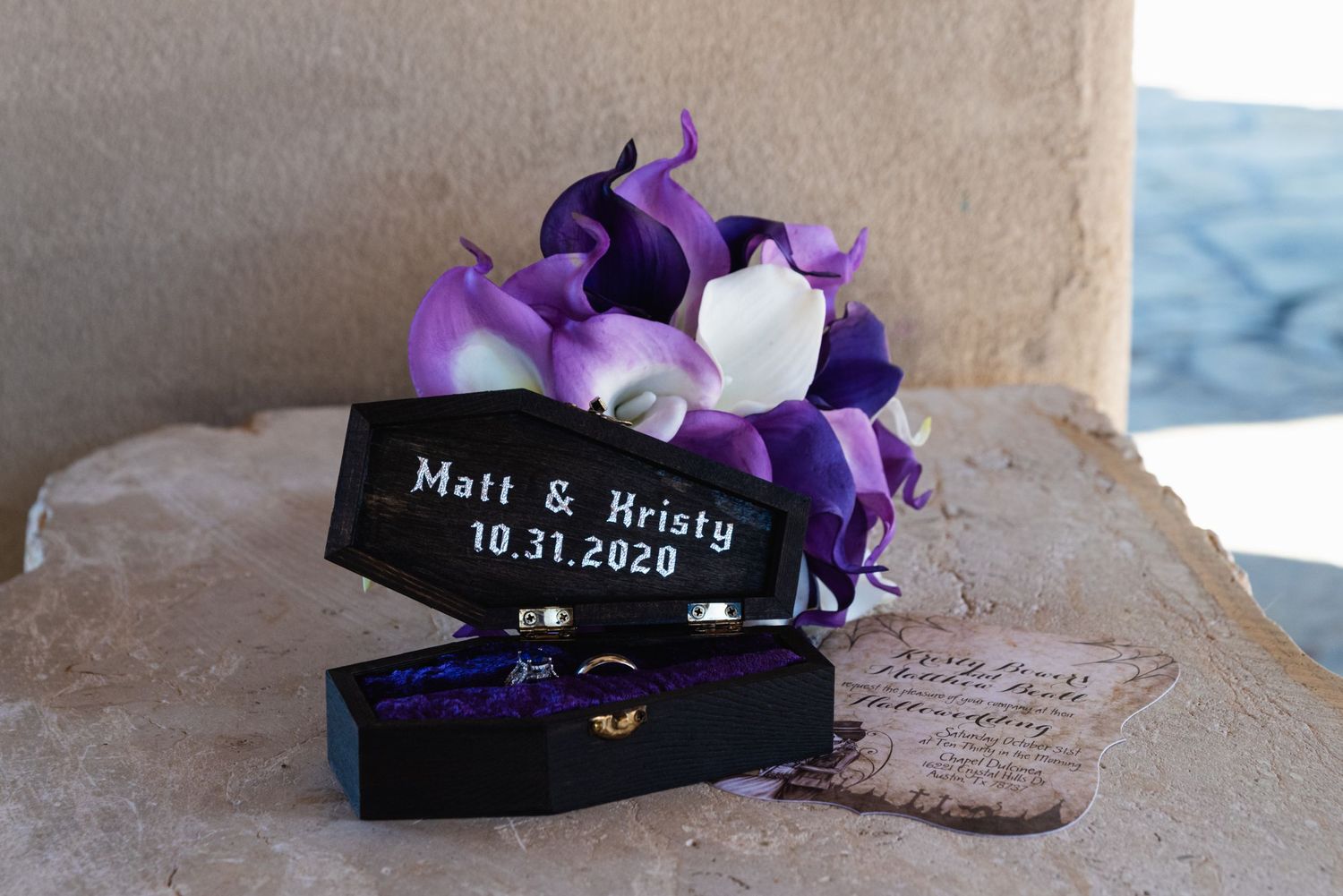 Purple and white floral arrangement with wedding date displayed on black card.