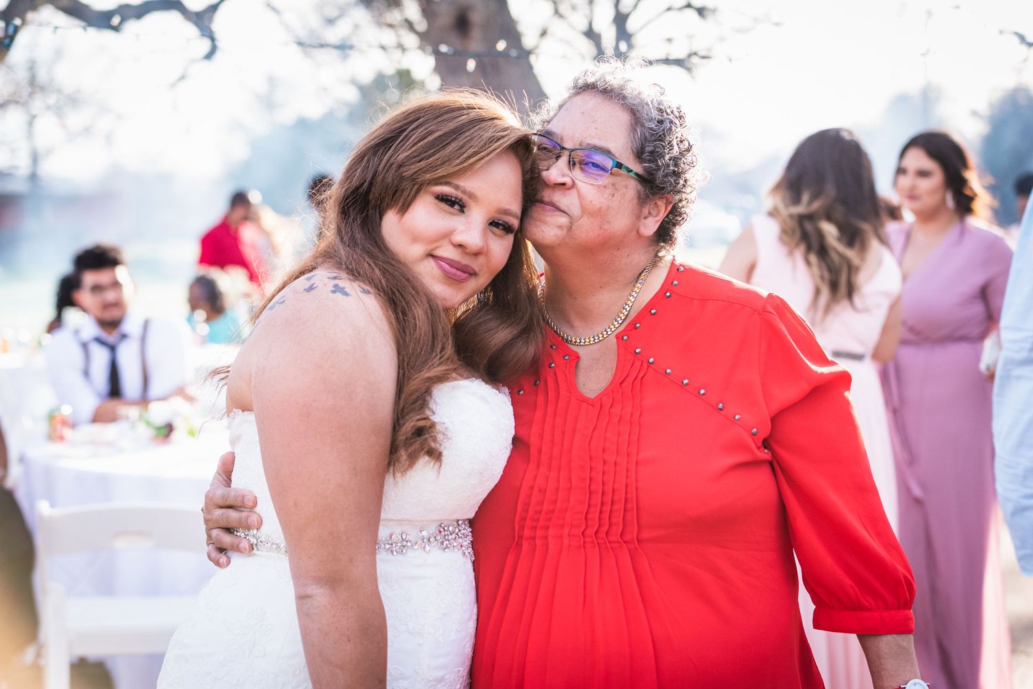 A heartwarming embrace shared between two wedding guests wearing red and white at an outdoor celebration.