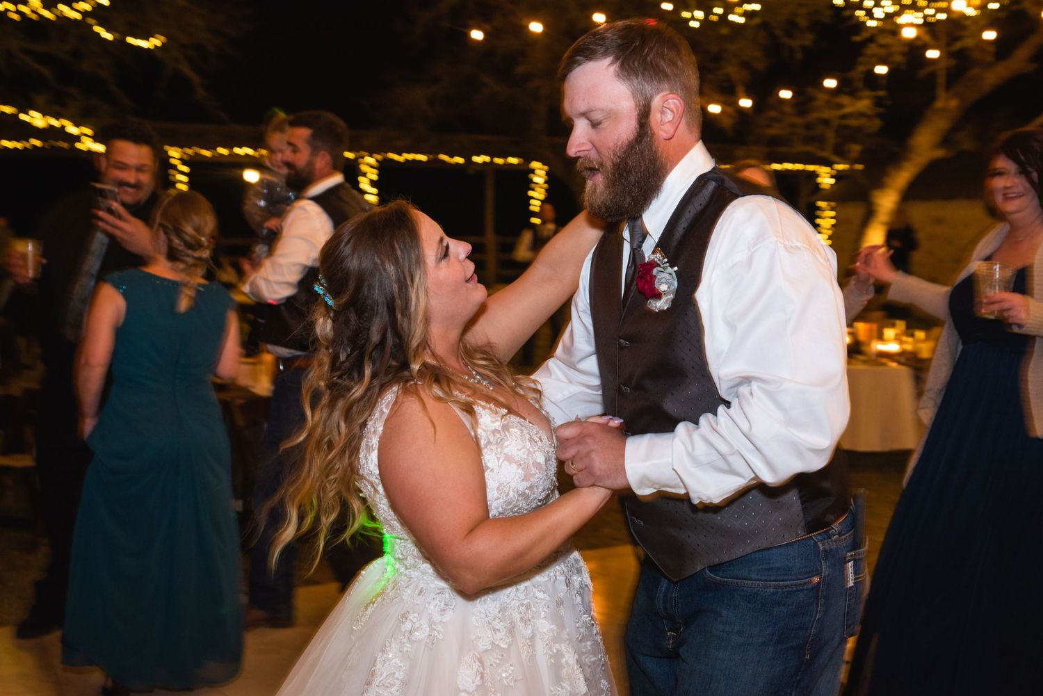 Dancing couple shares an intimate moment under string lights during their wedding reception.