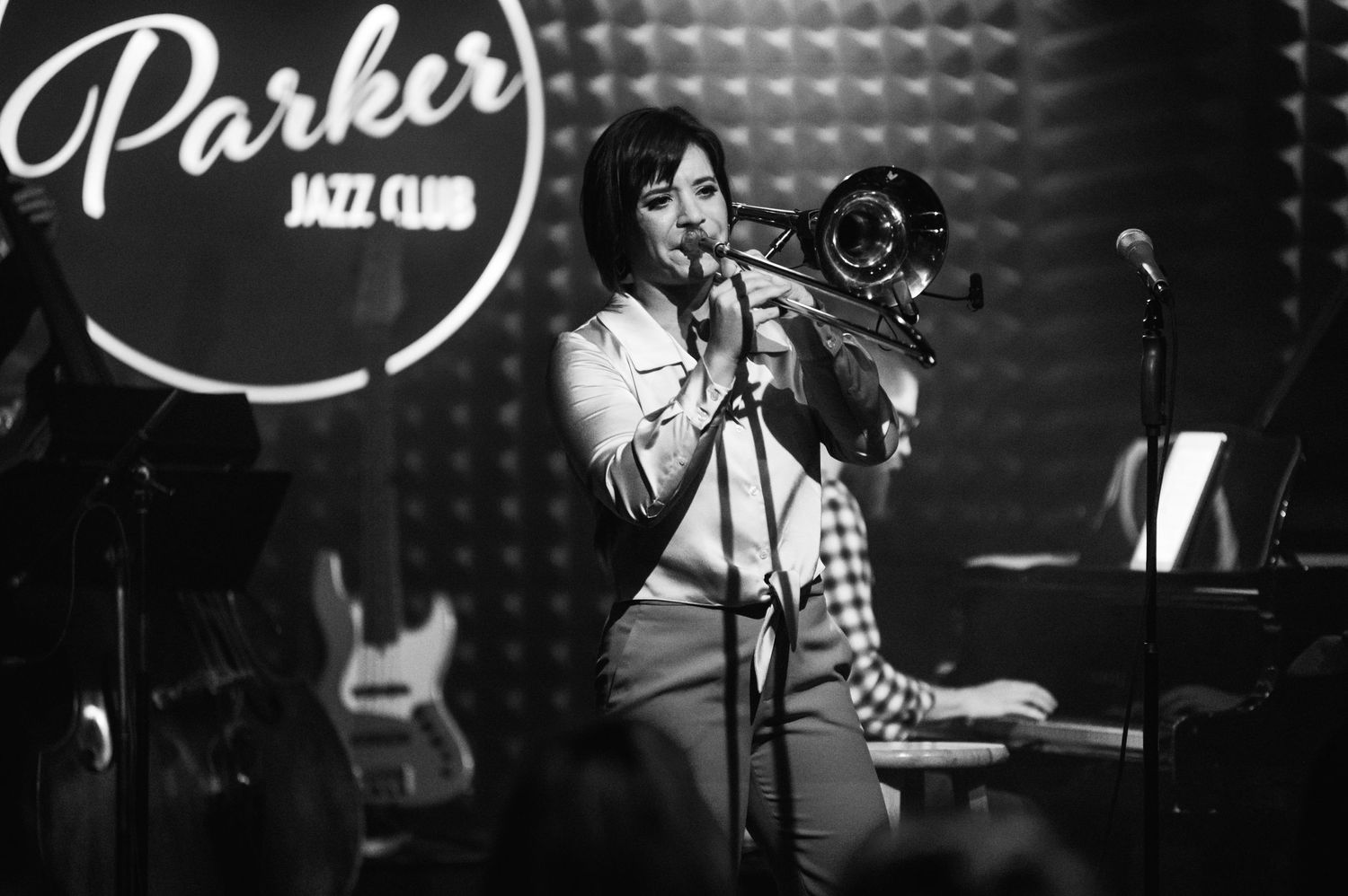 A performer plays trombone at Parker Jazz Club in black and white with dramatic lighting.