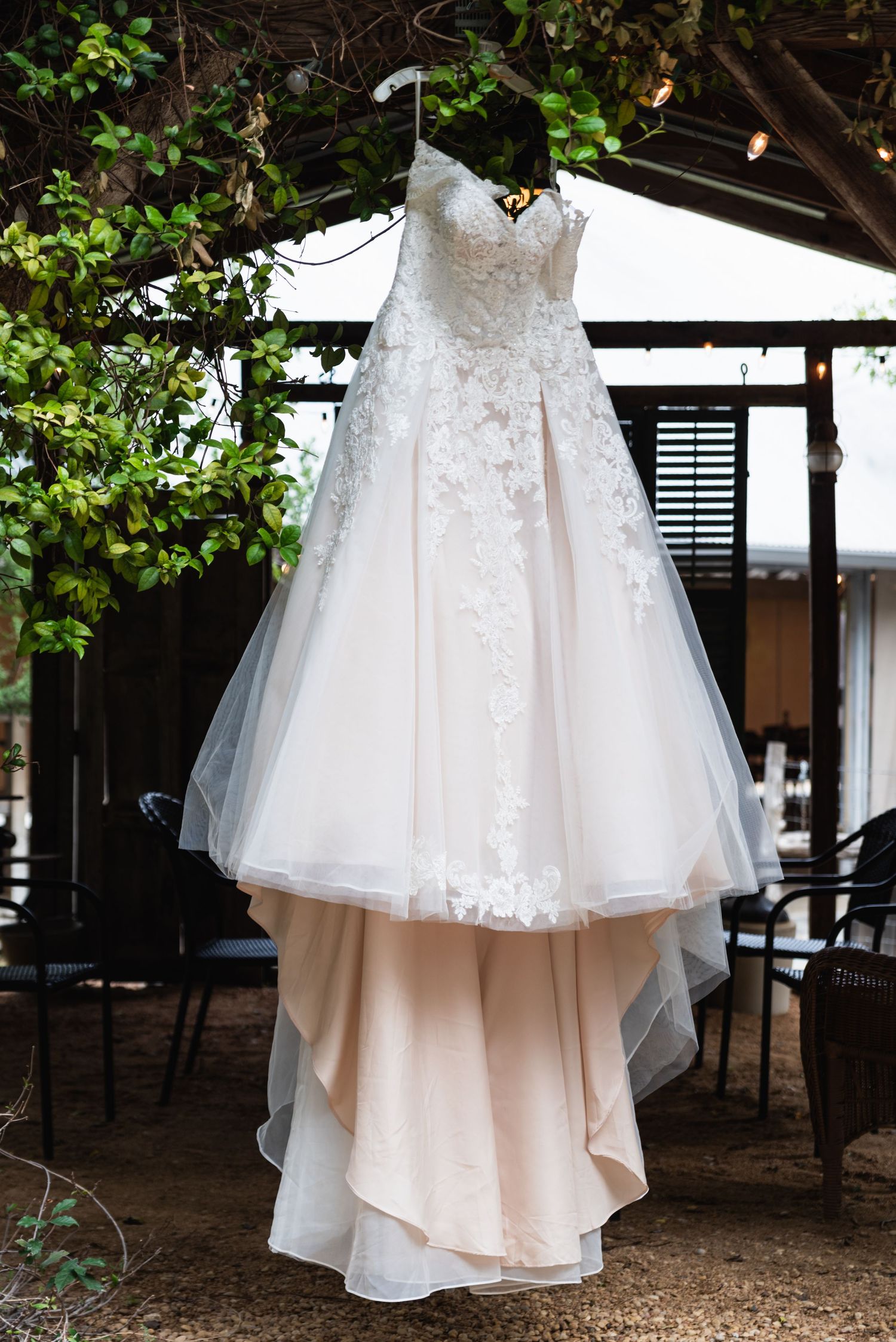 Elegant lace wedding dress with full tulle skirt hanging outdoors among green foliage.