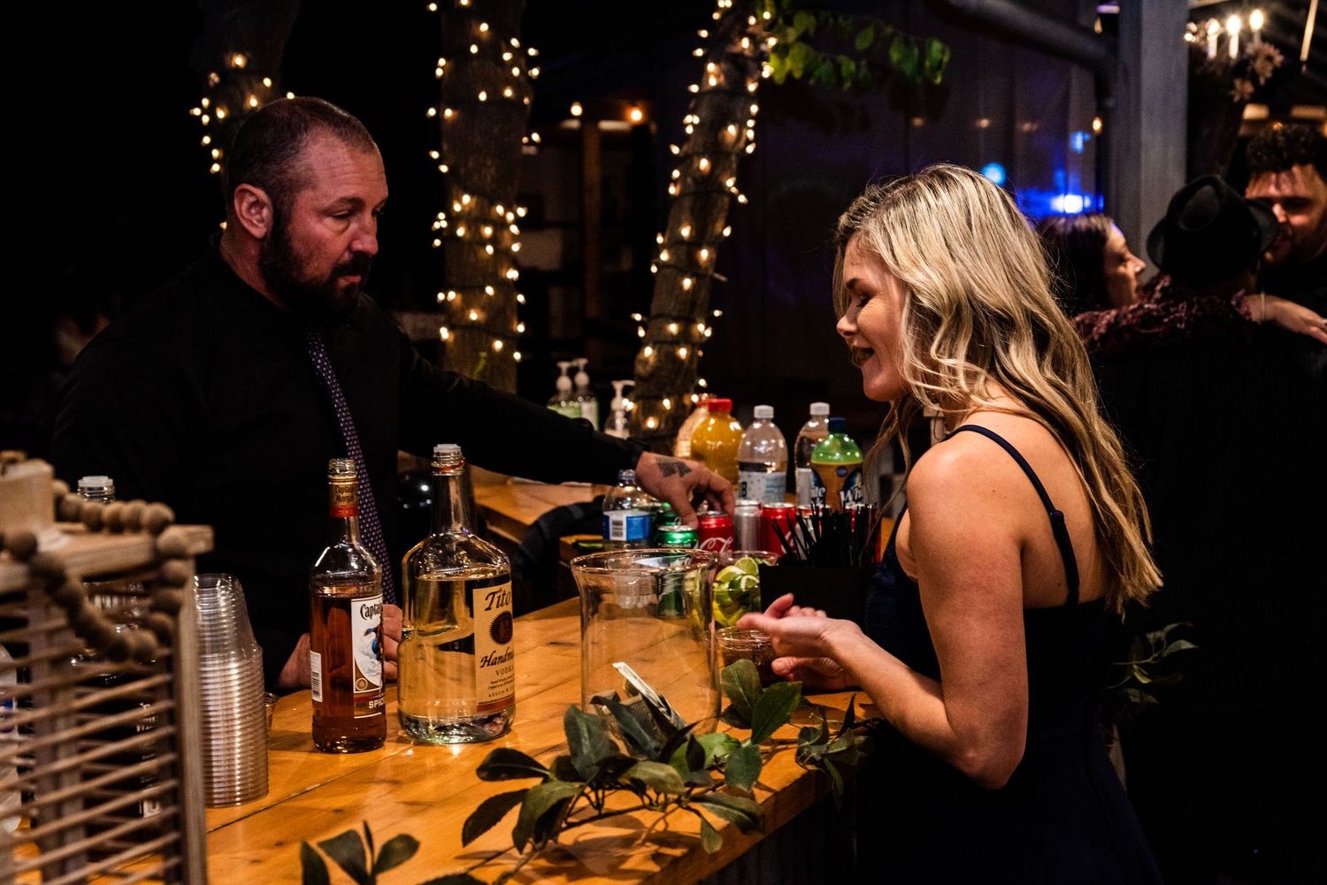 Guests enjoy drinks at a dimly lit bar decorated with string lights during an evening reception.