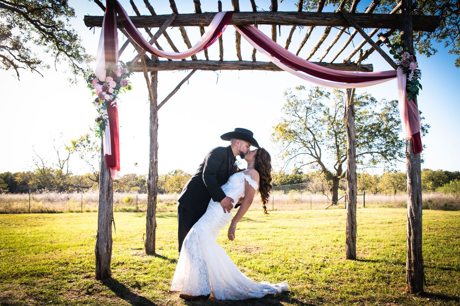 Romantic dip pose under wooden pergola during outdoor country wedding.