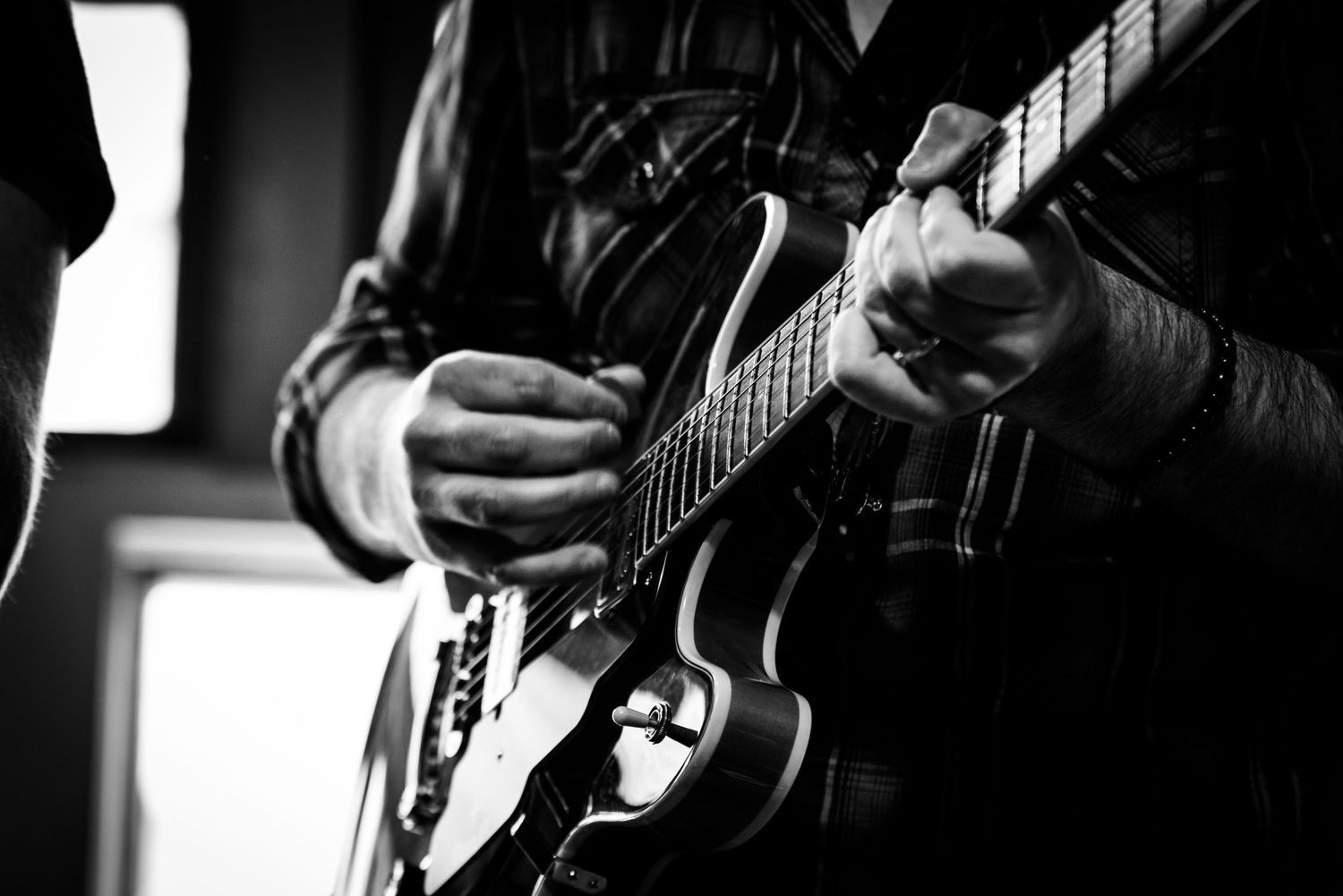 Close-up black and white shot of hands playing acoustic guitar, showing intricate fingerwork.