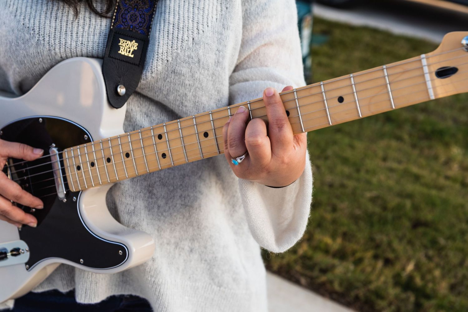 Close-up of hands playing a white Telecaster electric guitar with maple neck.