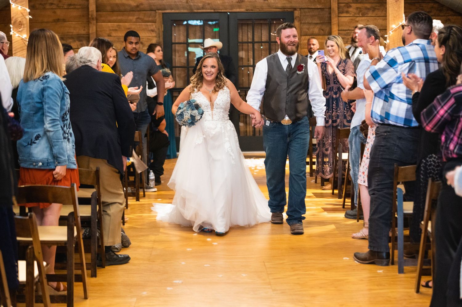 A newlywed couple makes their grand exit through the aisle of a wooden barn venue.