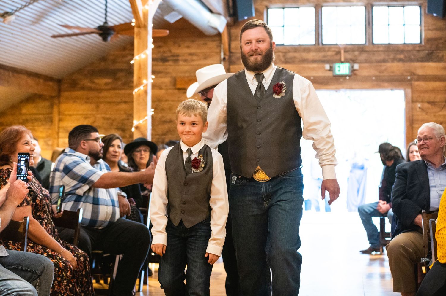 A processional walking down the aisle in a rustic barn-style wedding venue.