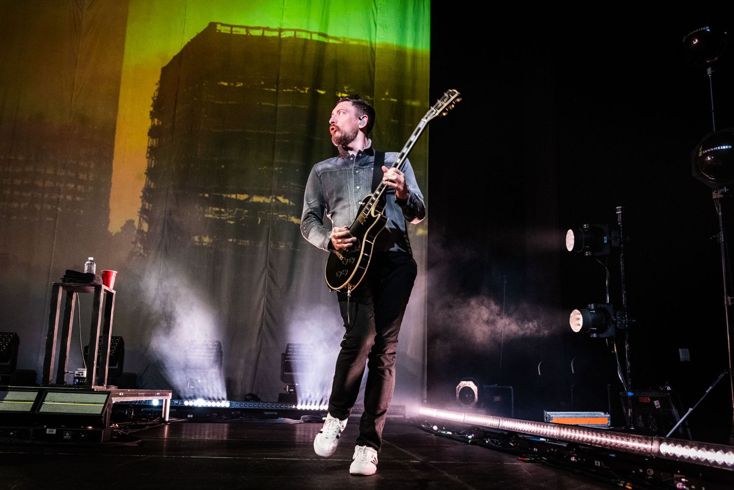 Musician plays electric guitar on misty concert stage with green lighting effects.