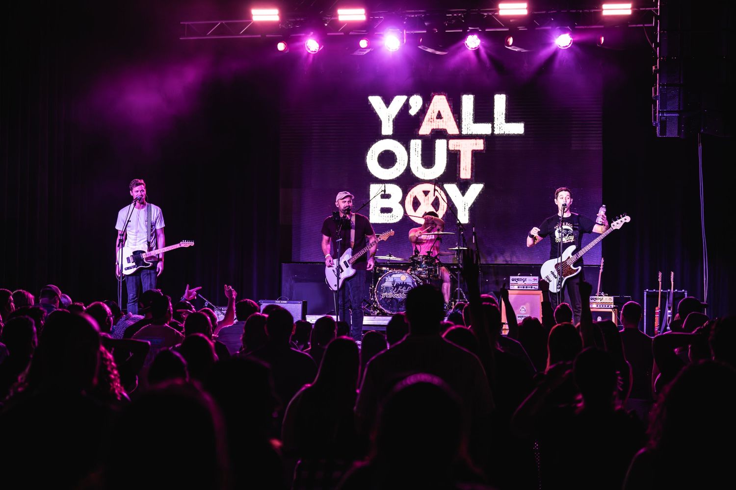 Band performs on stage with Y'ALL OUT BOY backdrop and purple stage lighting.