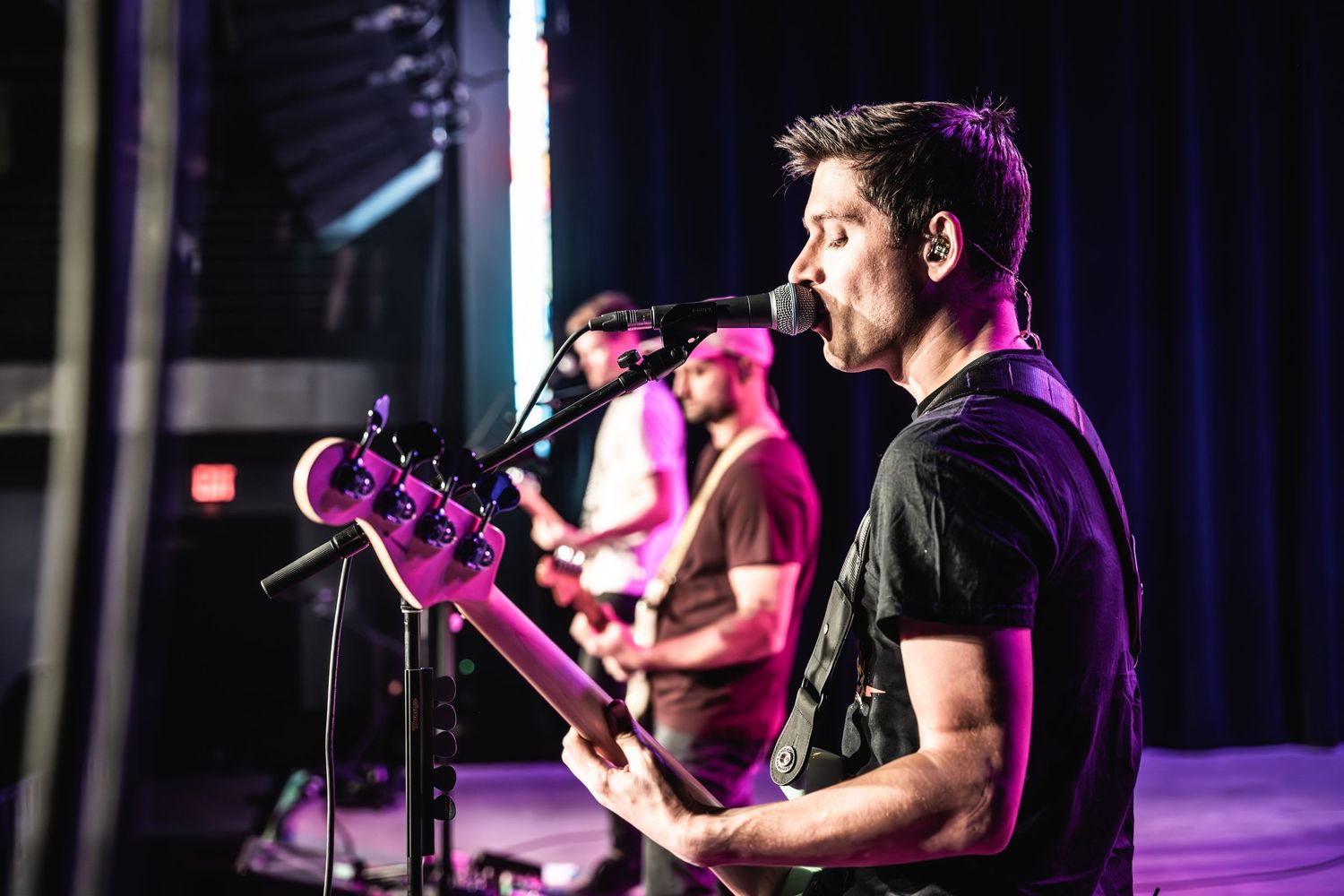 Musicians performing on stage with guitars under dramatic stage lighting.