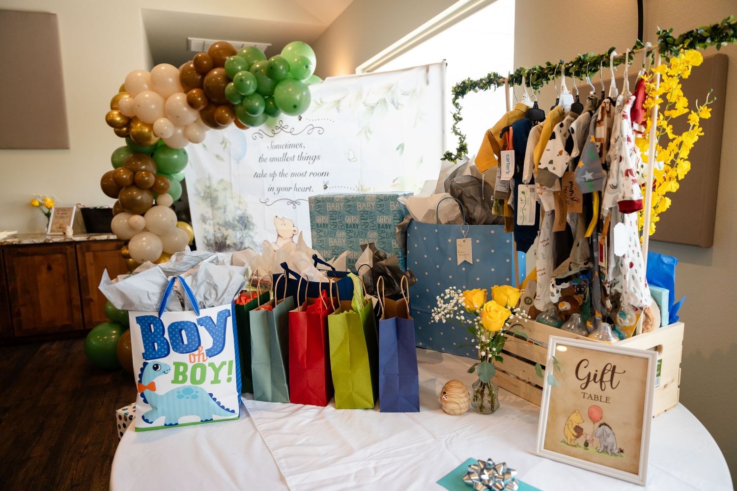 Baby shower gift table with balloon arch, colorful gift bags, and themed decorations.