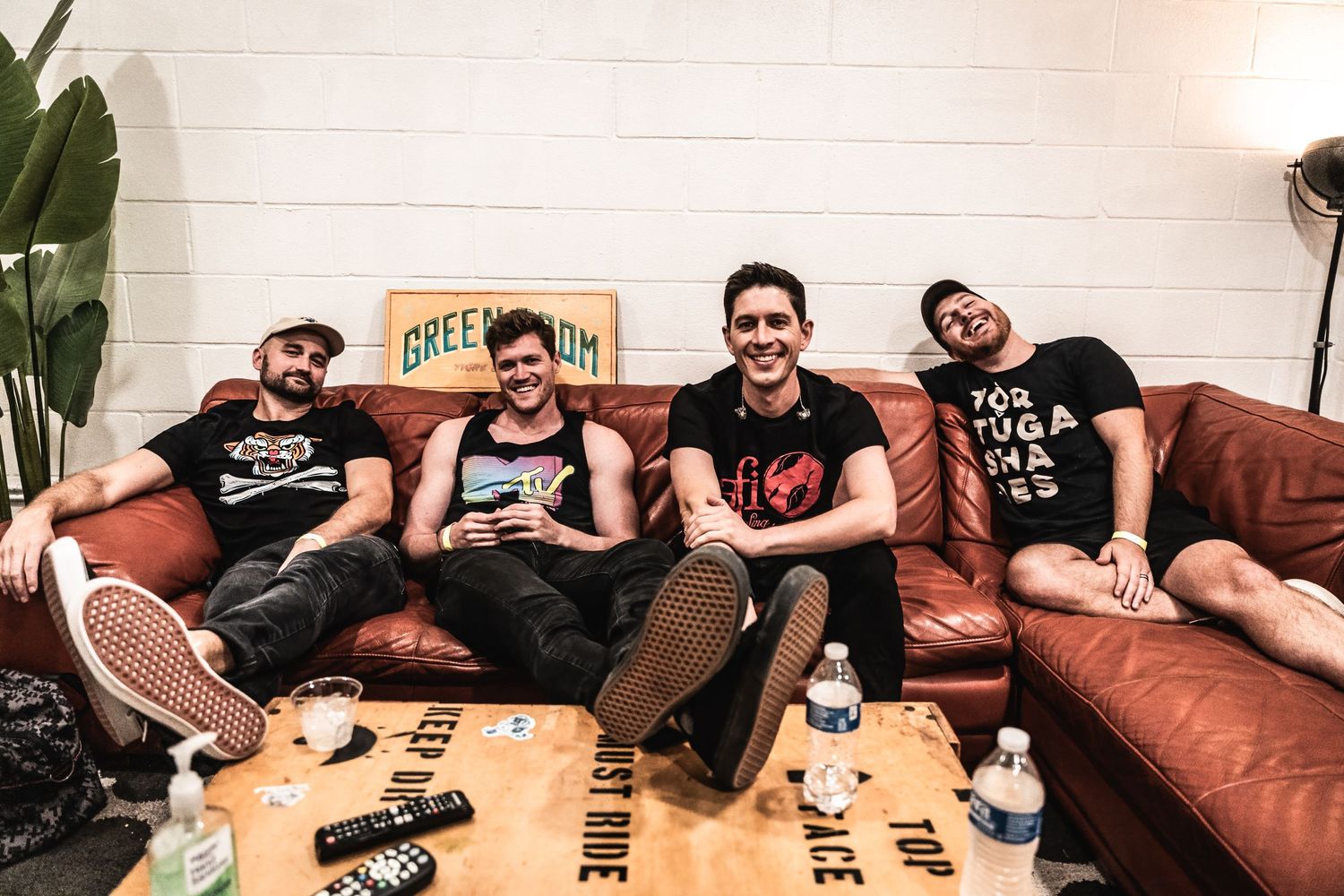 Musicians relax on brown leather couch during backstage break.