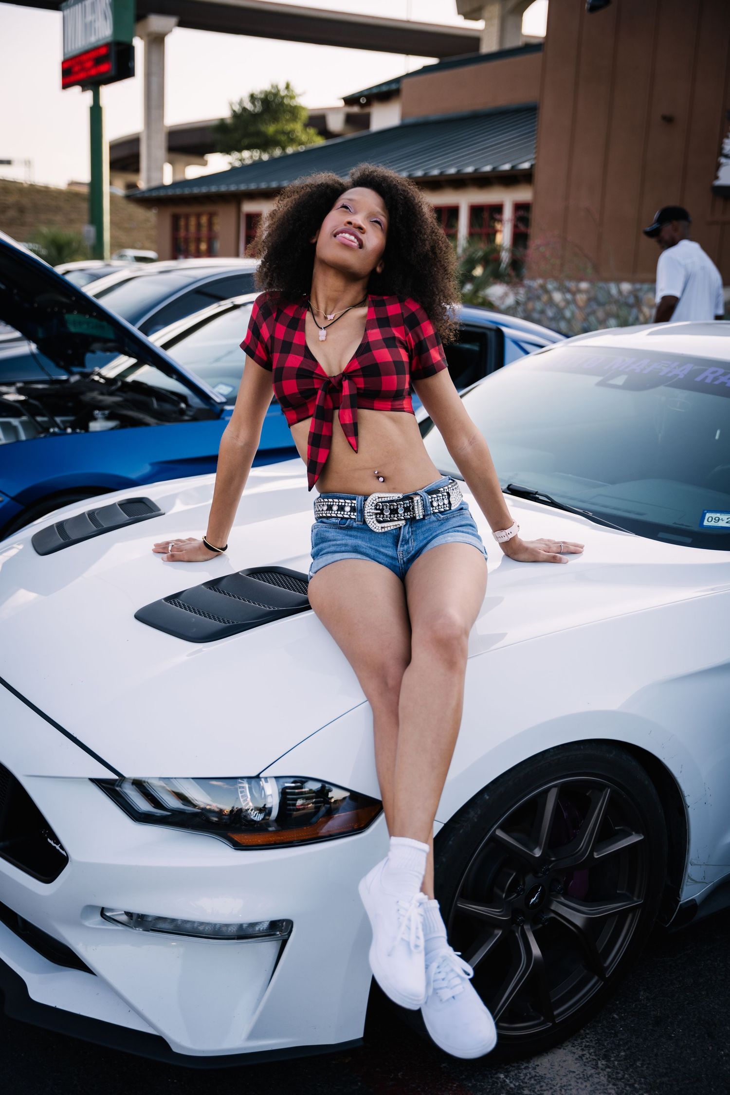 White Mustang GT on display at outdoor car meet with city backdrop.
