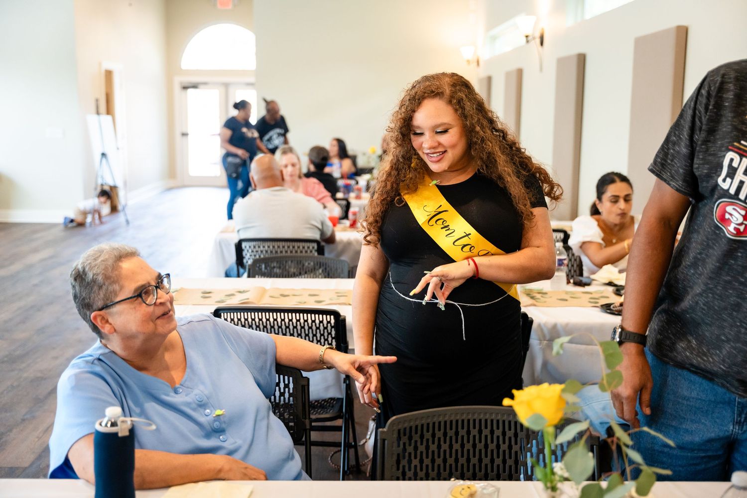 A person wearing a yellow sash interacts with guests during a baby shower celebration.