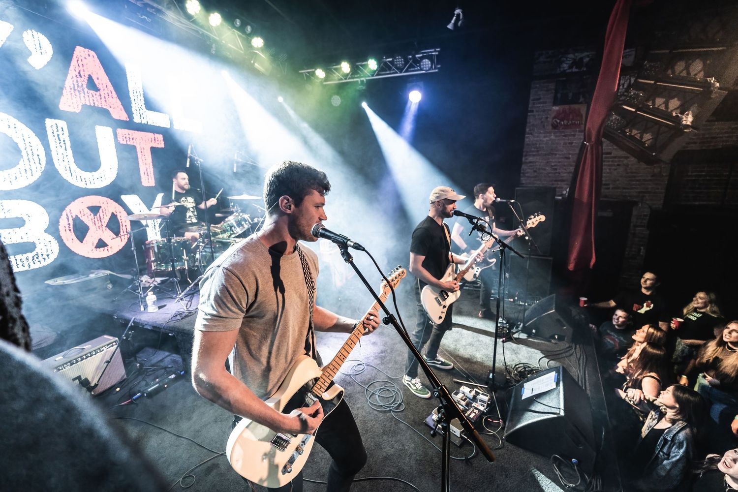 Rock band performs under dramatic stage lighting with Fall Out Boy signage visible above.