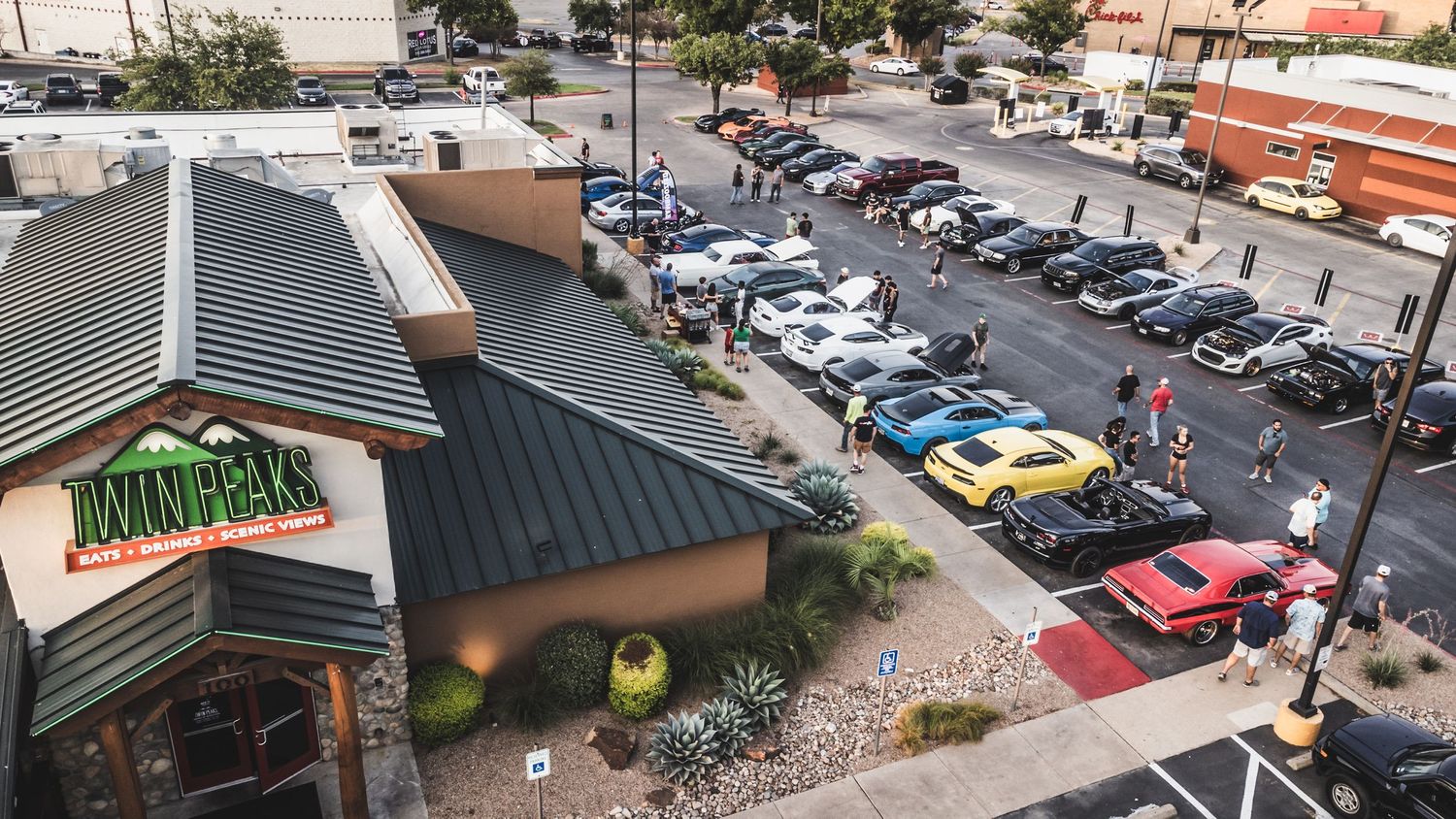 Mountain-themed restaurant exterior with parking lot full of classic and modern vehicles during car meet.