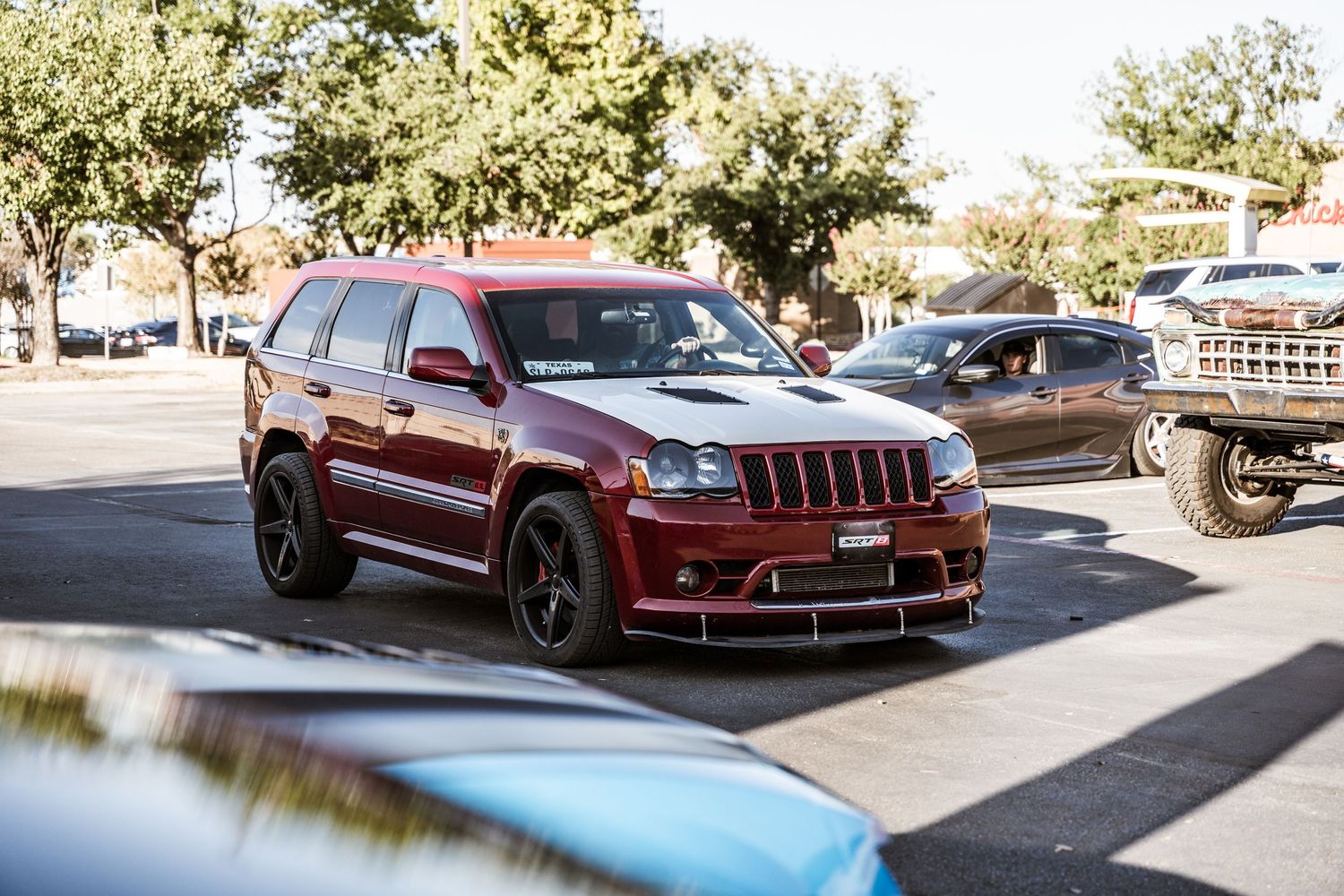 Modified maroon Jeep Grand Cherokee SRT with black wheels parked in a lot.