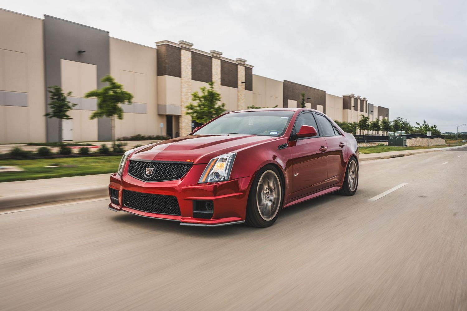 Red Cadillac CTS-V sedan in motion on a street with industrial buildings in the background.