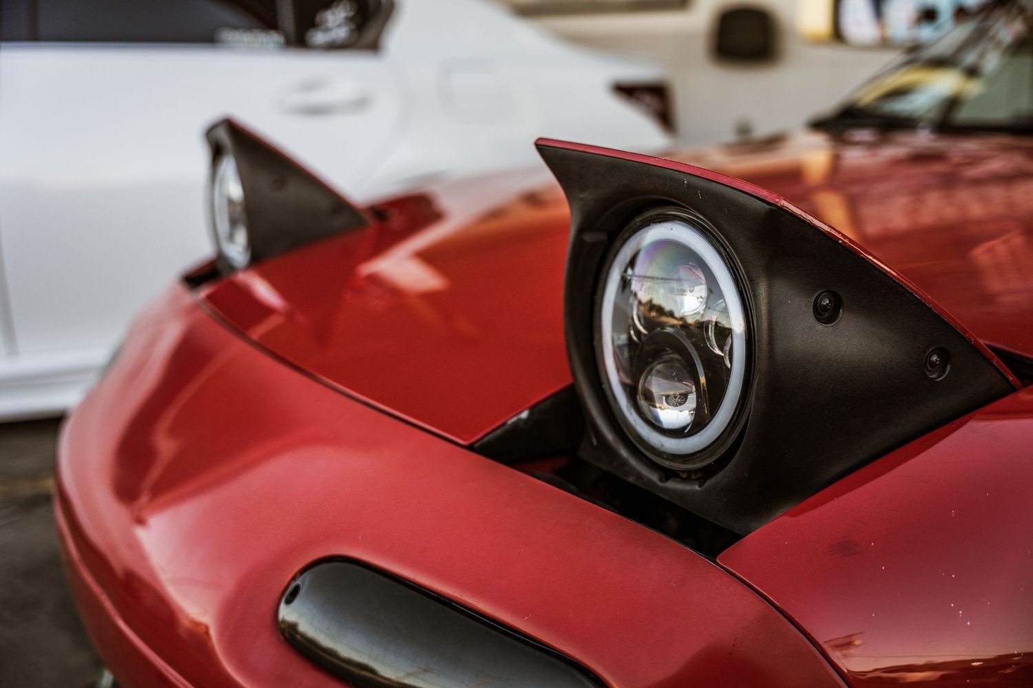 Close-up of a red sports car's pop-up headlight housing with modern LED lighting.