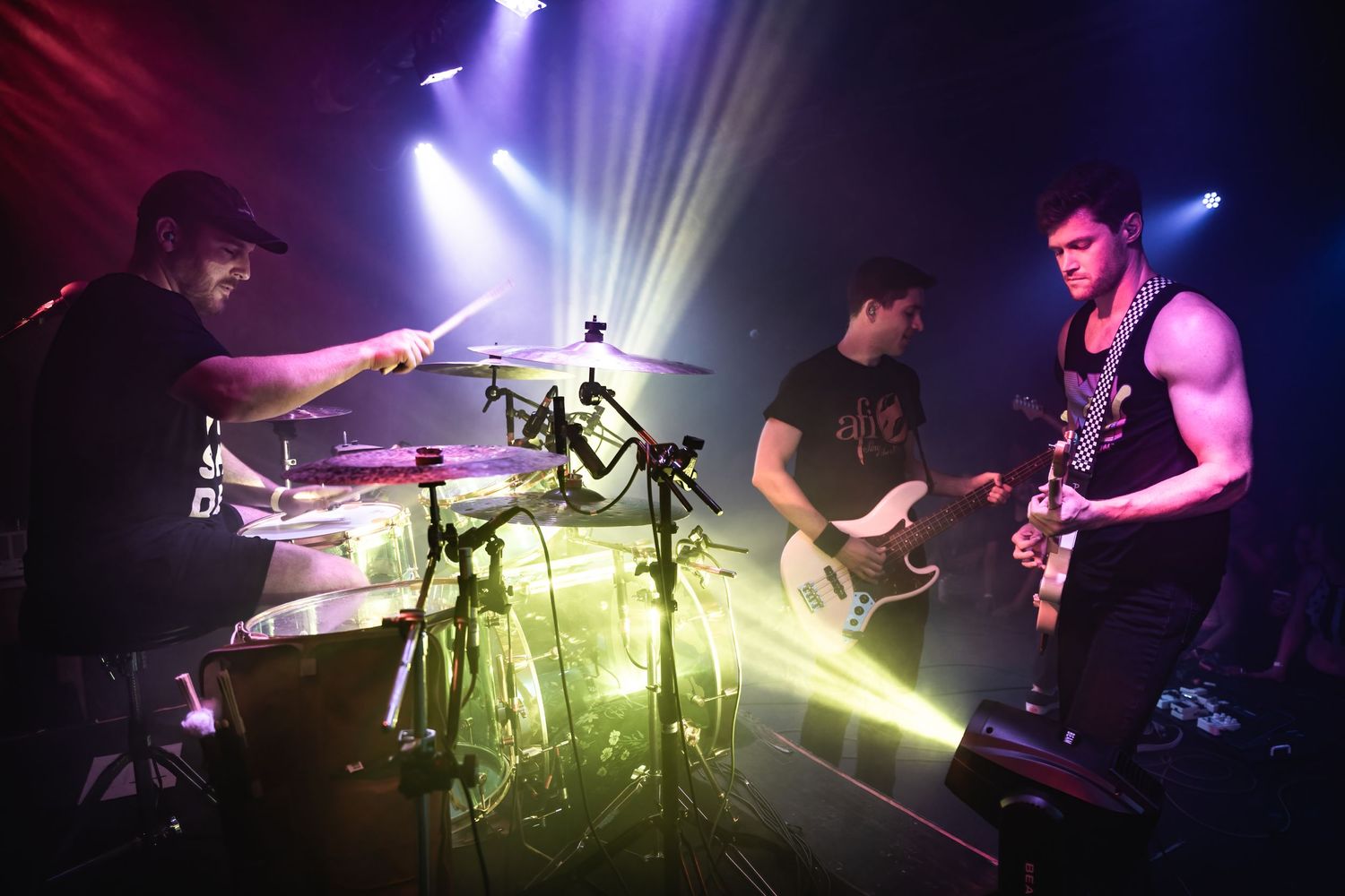 Band performing on stage with dramatic lighting and drum kit in foreground.
