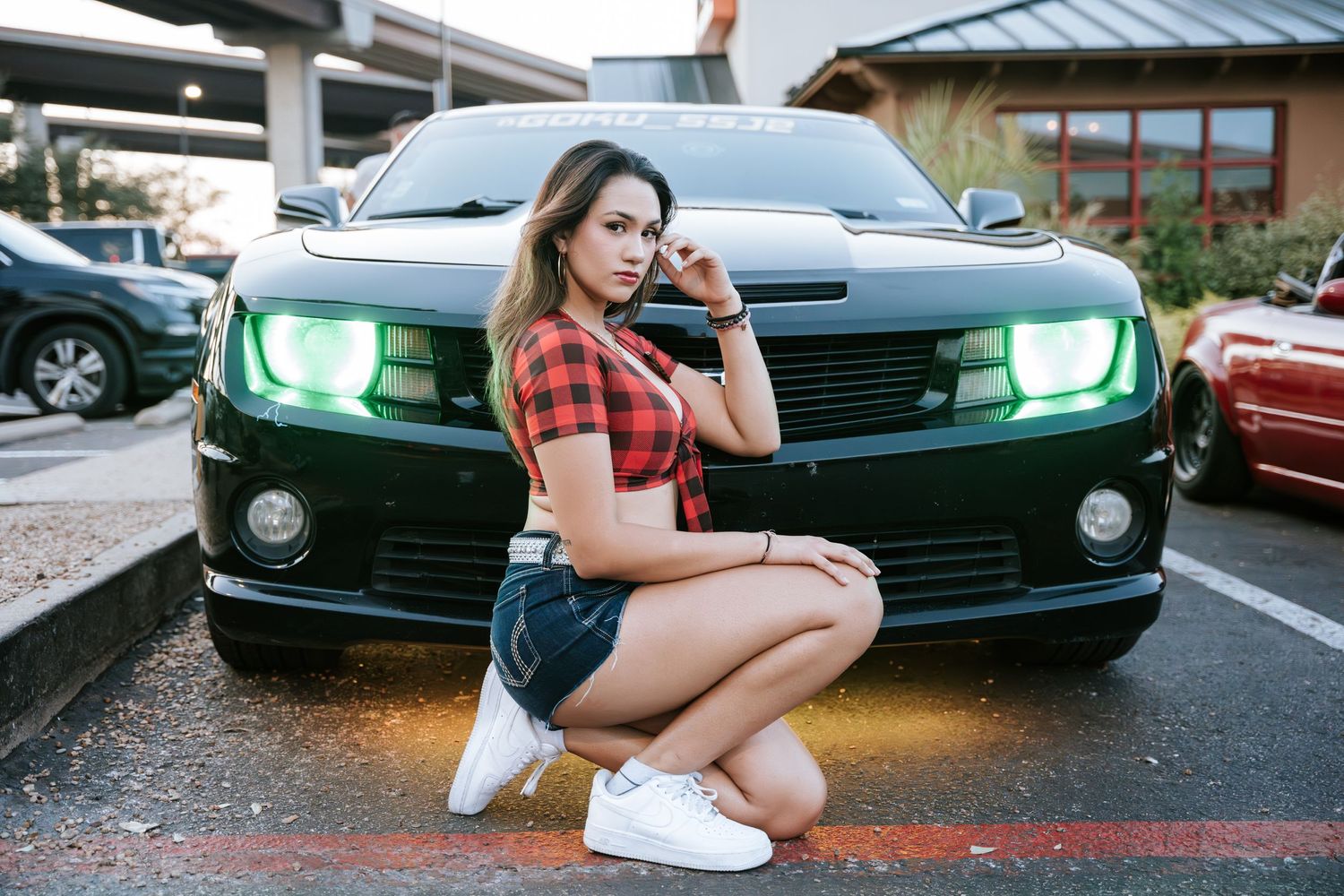 Car enthusiast photoshoot with green-lit Camaro headlights in evening setting.