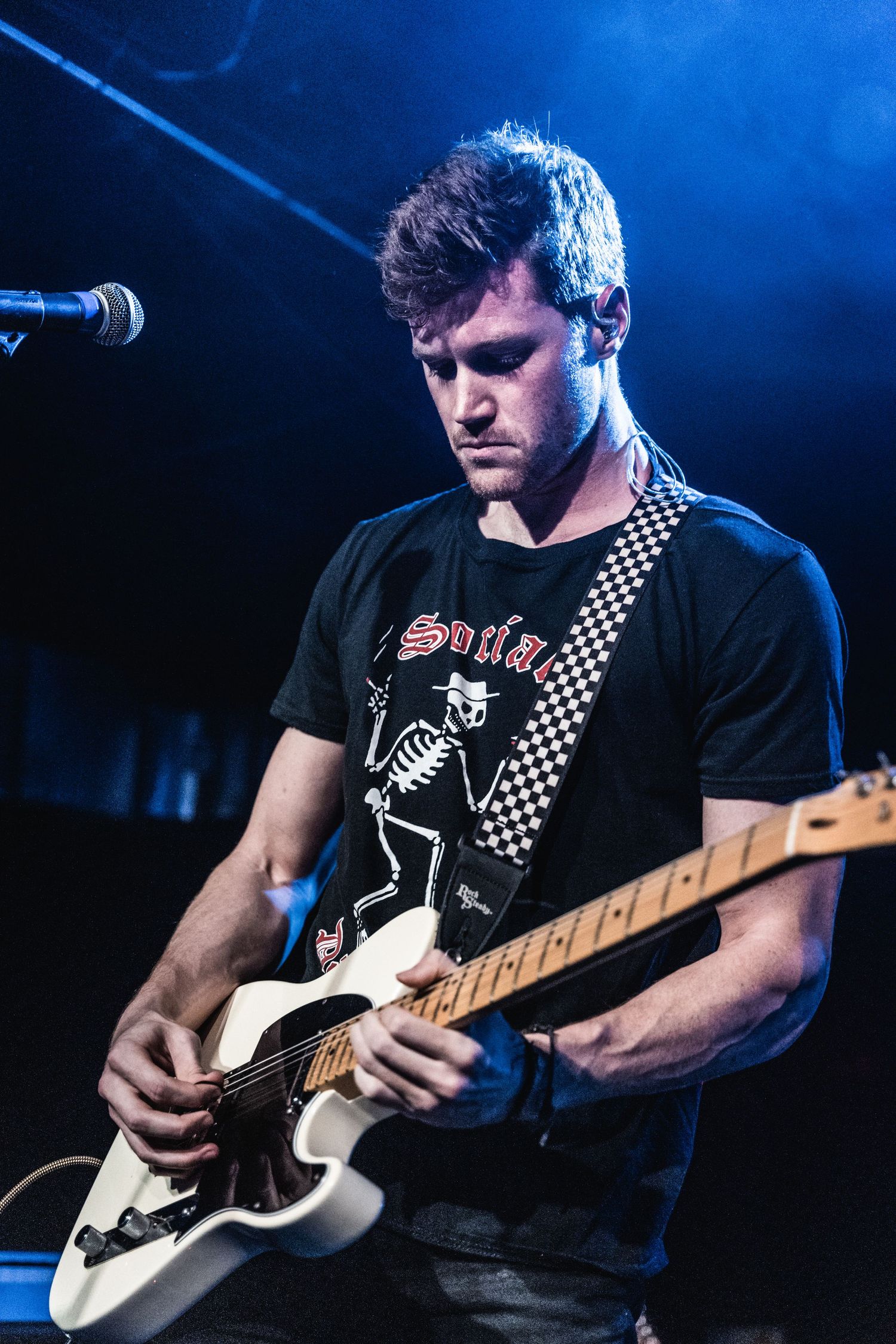 Musician plays white electric guitar while performing in black t-shirt with skeleton design.