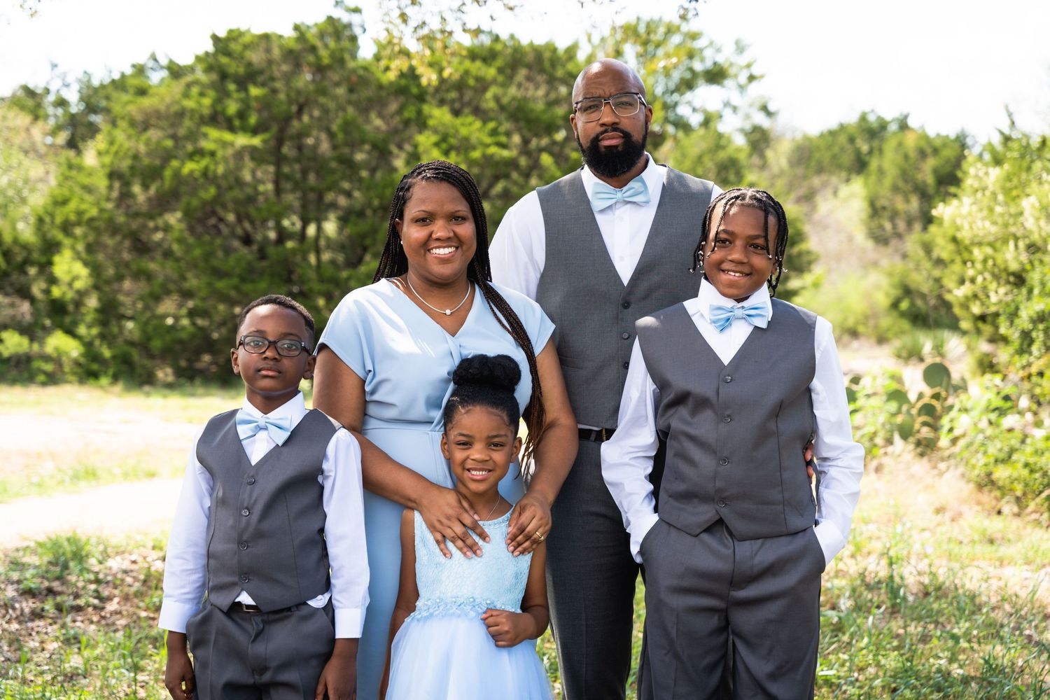 Family group wearing coordinated formal attire poses together outside in natural setting.