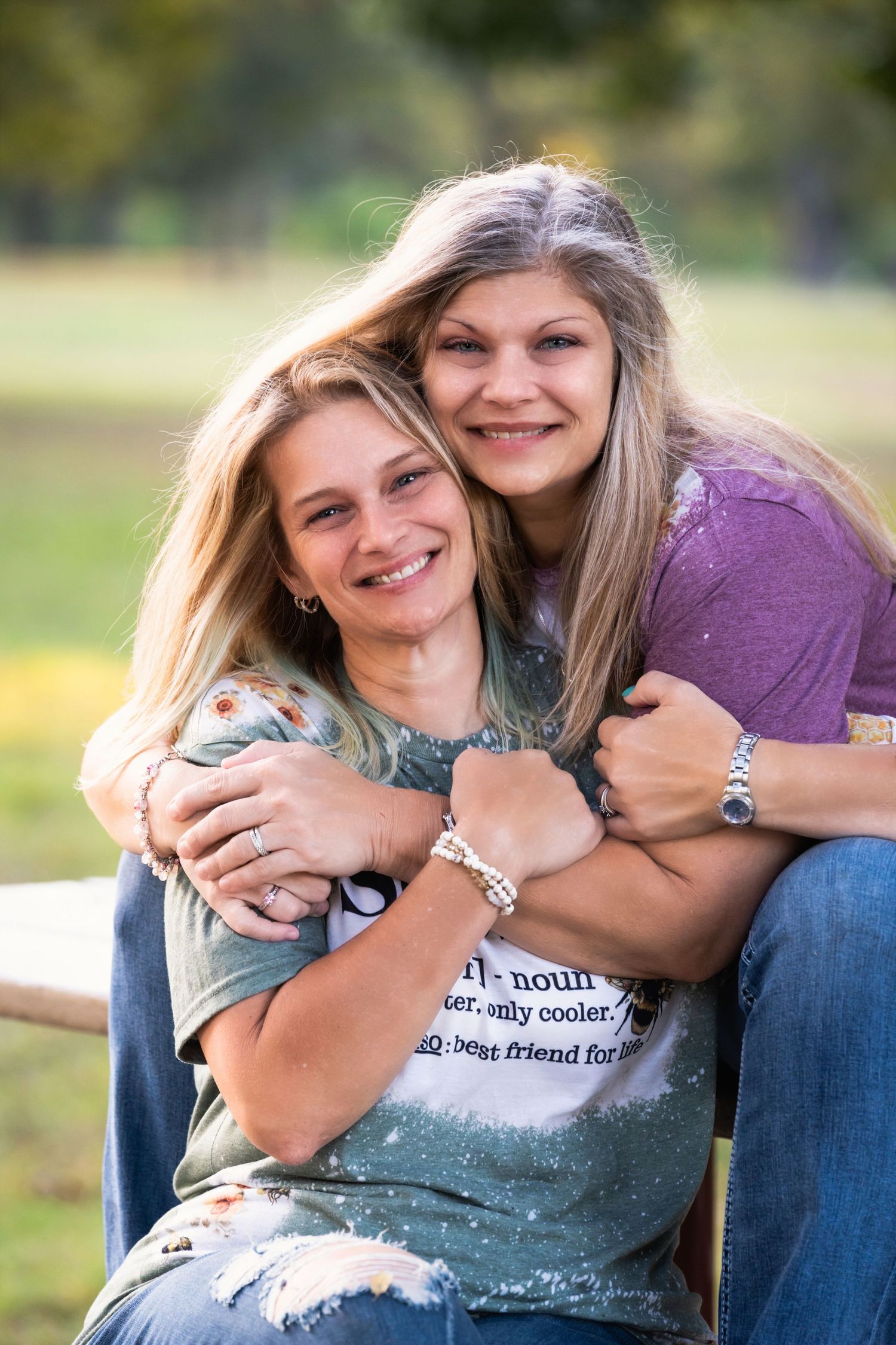 Two friends sharing a joyful moment while embracing outdoors during a sunny day photoshoot.