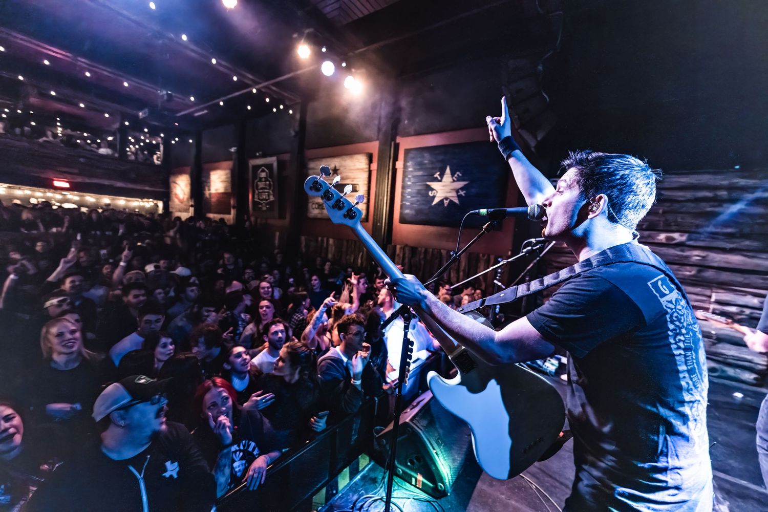 Performer on stage reaches out to crowd during energetic concert in packed venue.