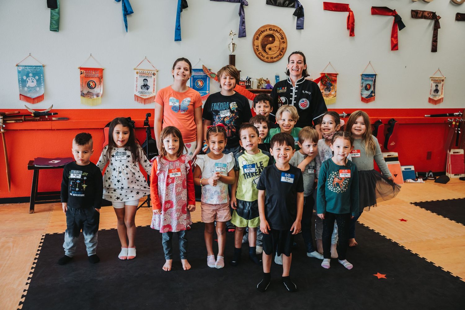Group photo of martial arts students standing together in front of colorful belt display.