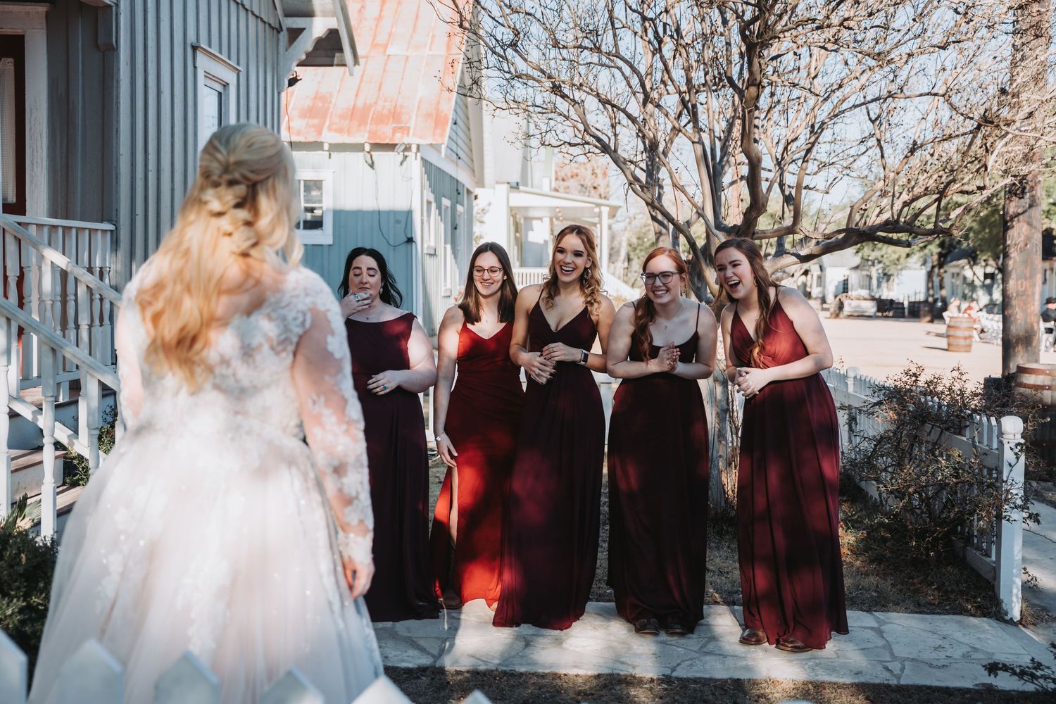 A wedding party gathers outside with bridesmaids wearing burgundy dresses.