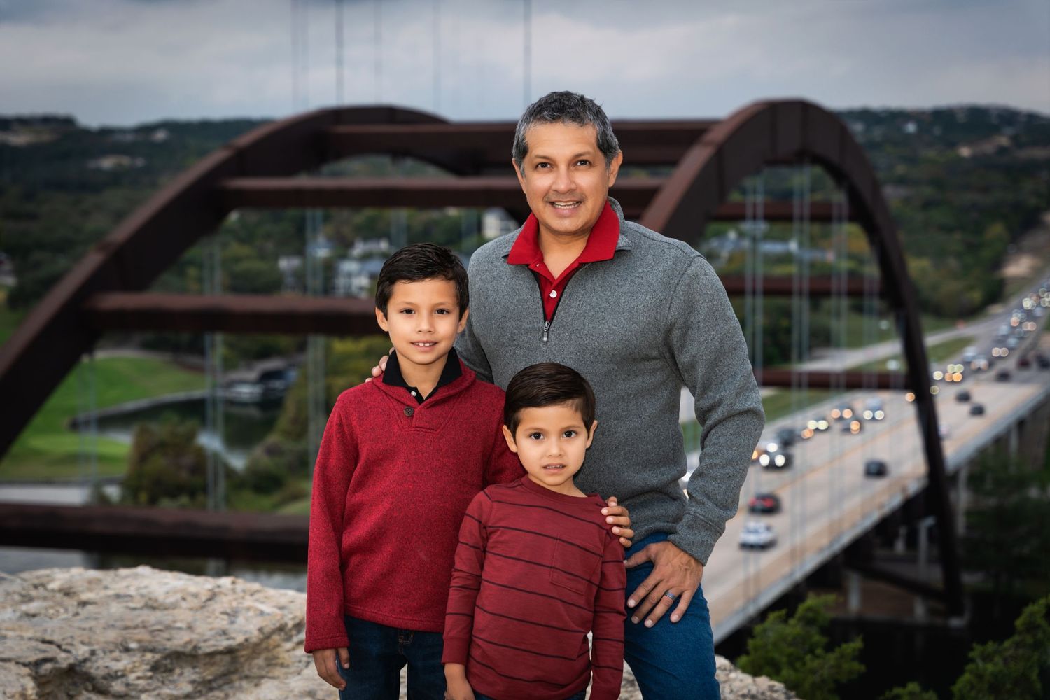 Group portrait against scenic backdrop of Pennybacker Bridge in Austin during cloudy day.