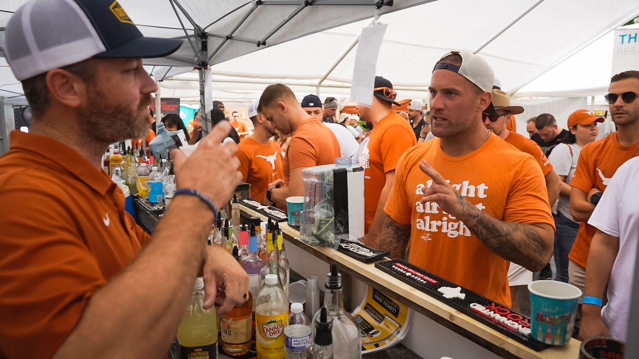 Bartenders serving drinks at outdoor event with orange-shirted attendees.