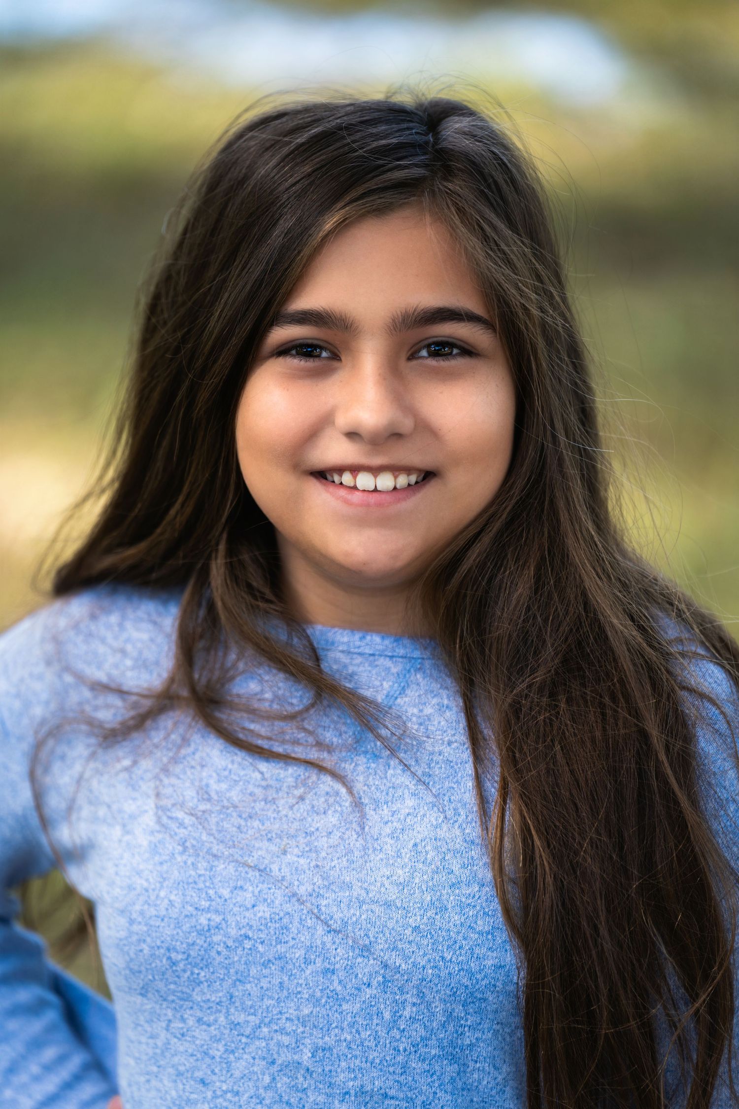 Portrait of young person in blue sweater against blurred natural background.