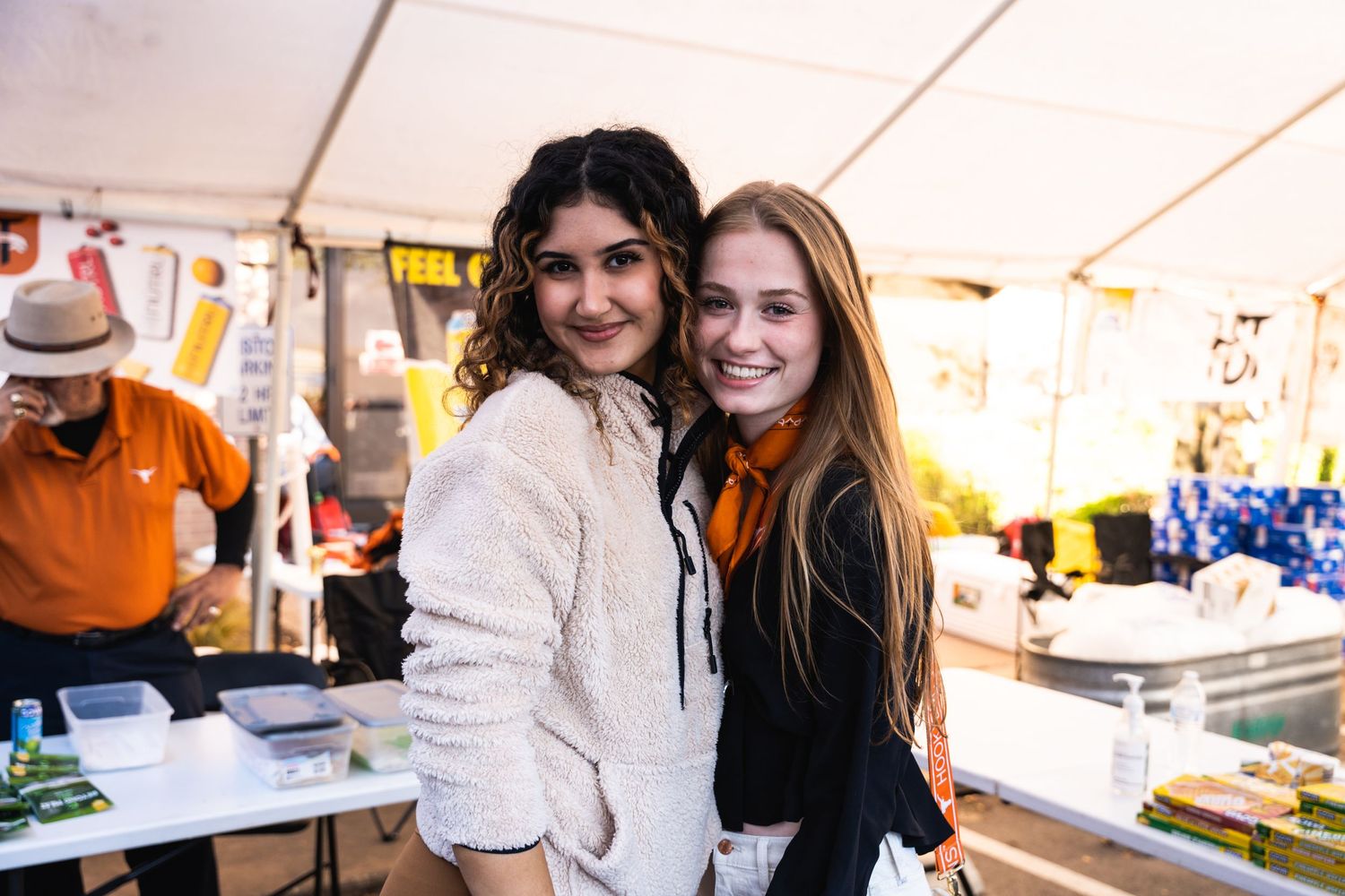 Two friends posing together at an outdoor event under a white tent.
