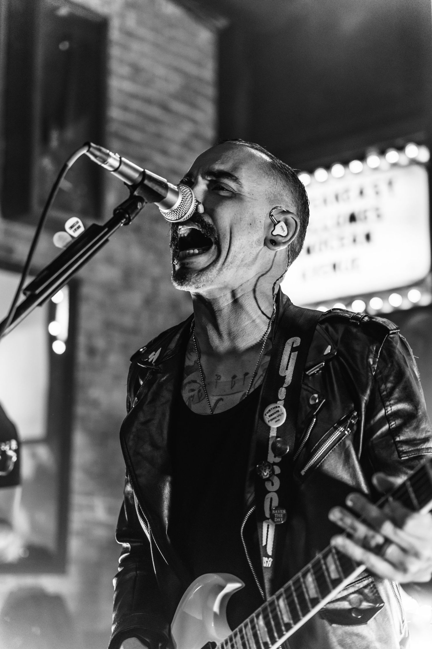 Black and white photo of performer singing intensely into microphone while playing guitar.