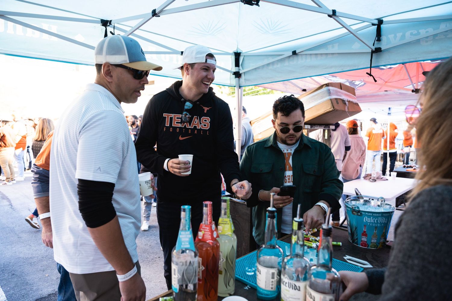 Group gathered around a beverage tasting tent with various bottles on display at an outdoor event.