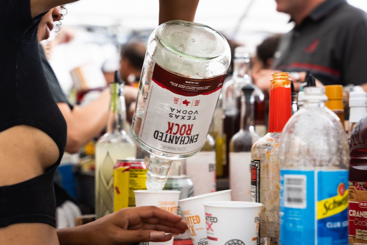 A hand holds up a can of beer among various drinks and beverages at an outdoor gathering.