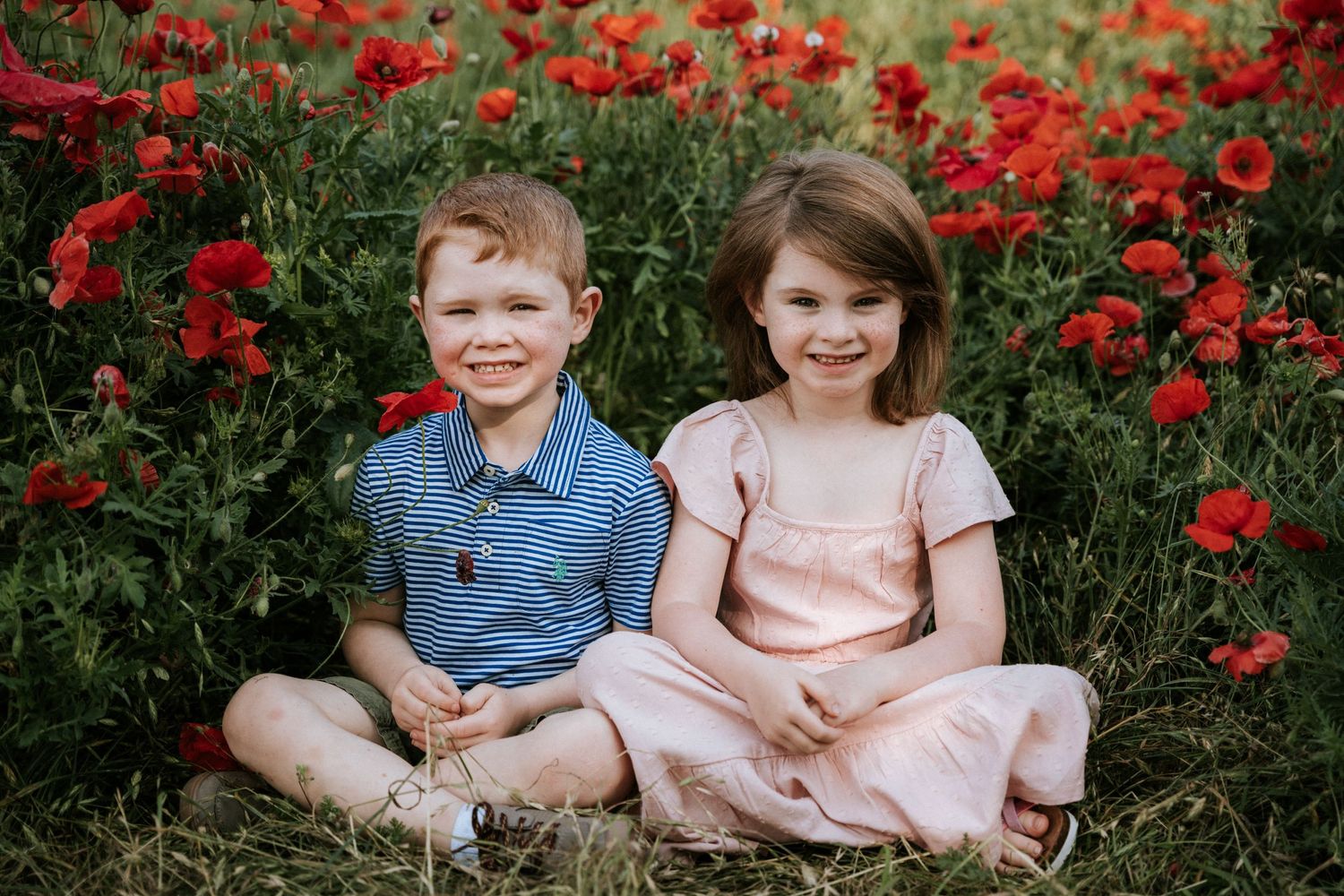 Two children sit together in a blooming field of red poppies.