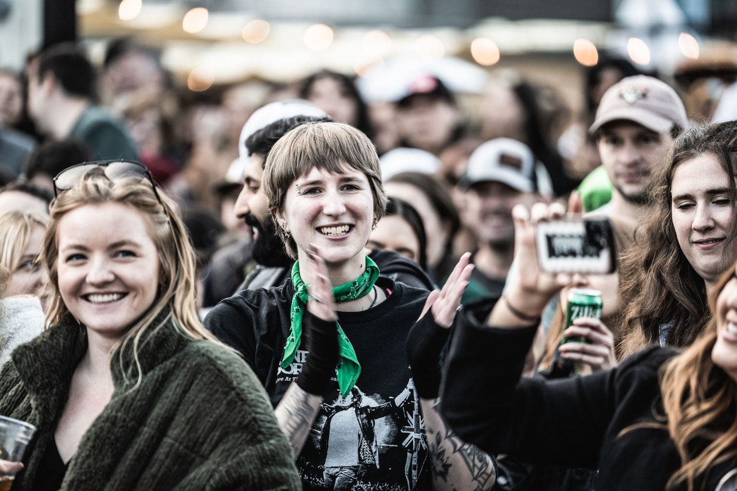 Excited crowd members enjoying a festive outdoor event with string lights and decorations visible in the background.